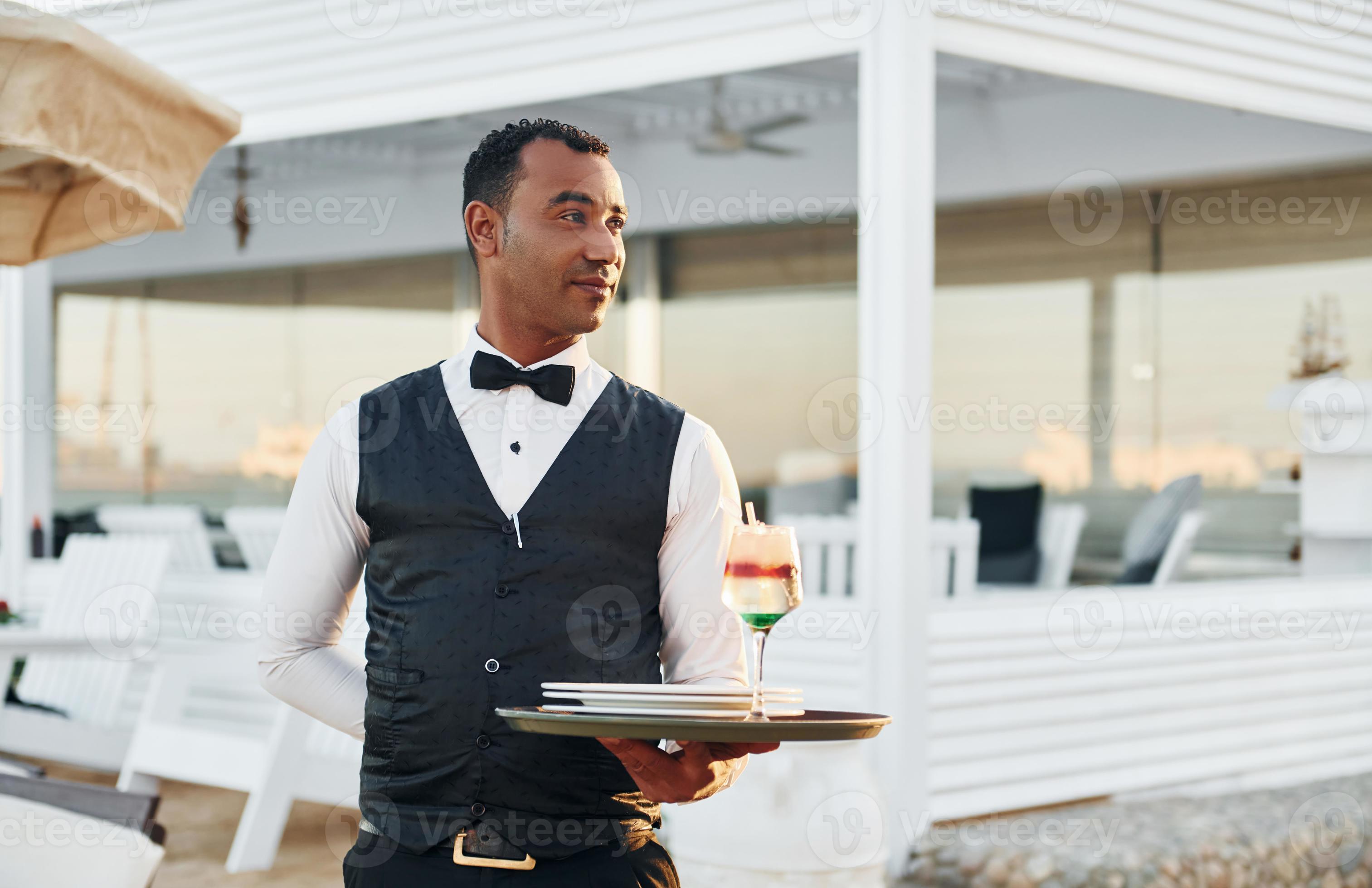 With order in hand Black waiter in formal clothes is at his work With order in hand Black waiter in formal clothes is at his work