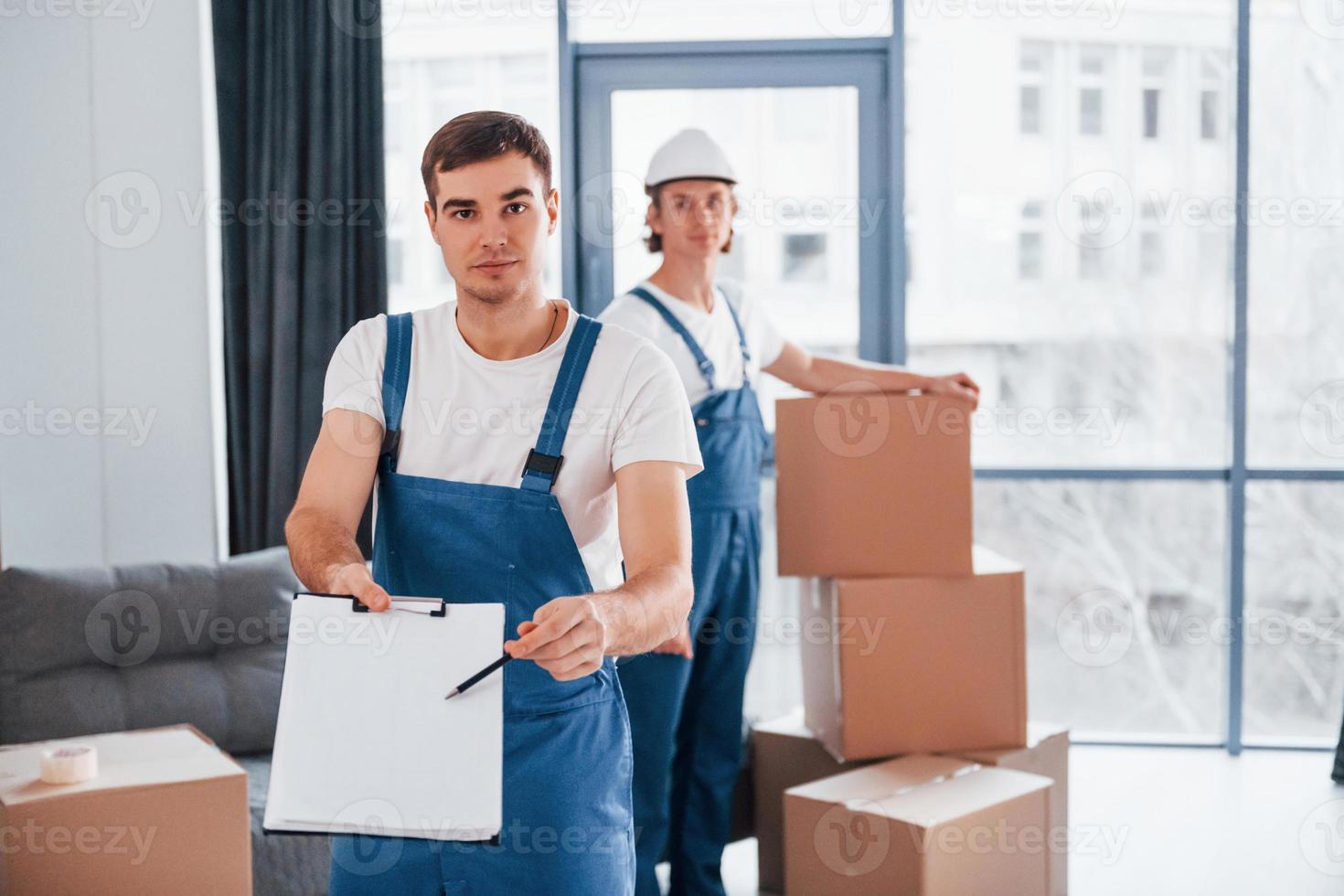 Document to sign. Two young movers in blue uniform working indoors in the room photo