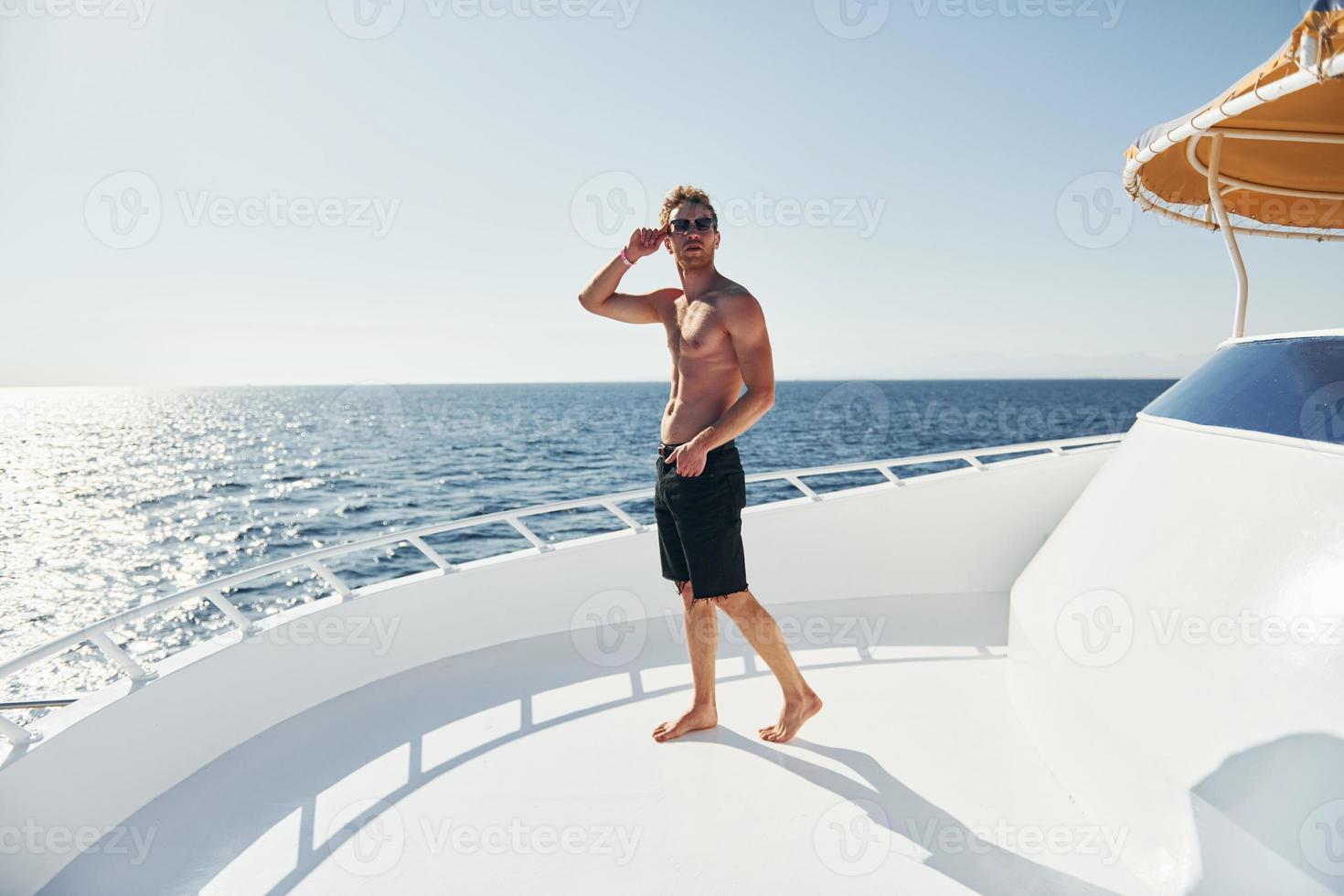 In sunglasses. Young male tourist is on the yacht on the sea. Conception of vacation photo