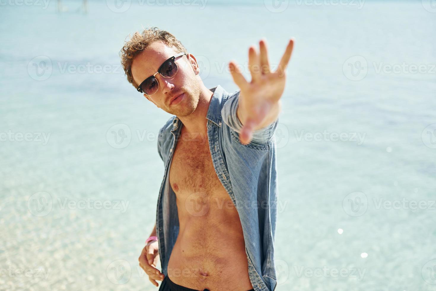 In sunglasses. Young european man have vacation and enjoying free time on the beach of sea photo