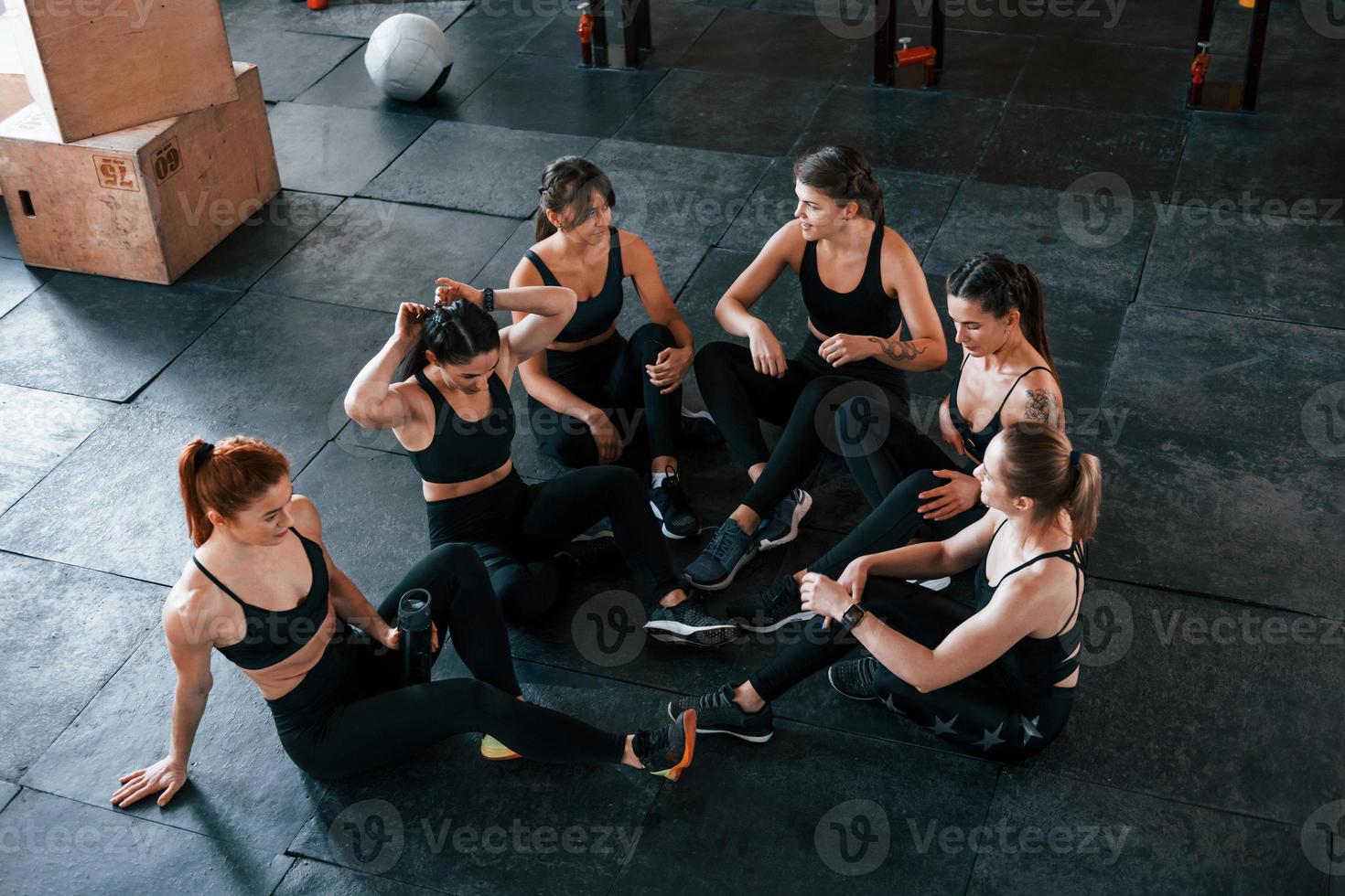 Sitting on floor. Group of young sportive people have crossfit day indoors in gym photo