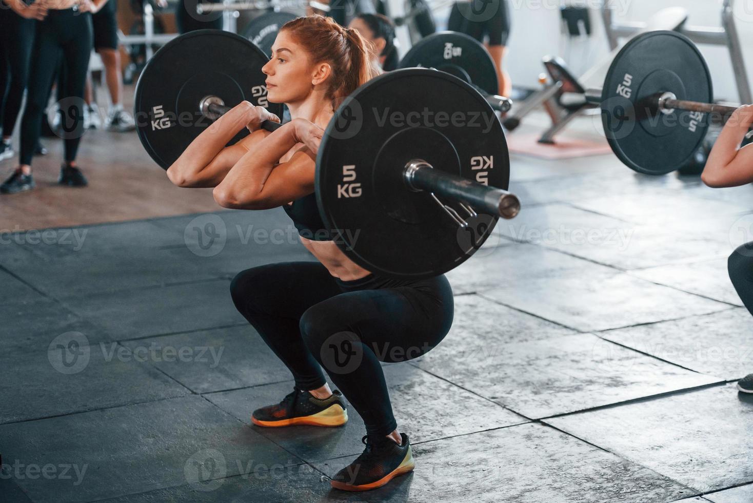 Lifting barbell. Group of young sportive people have crossfit day indoors in gym photo