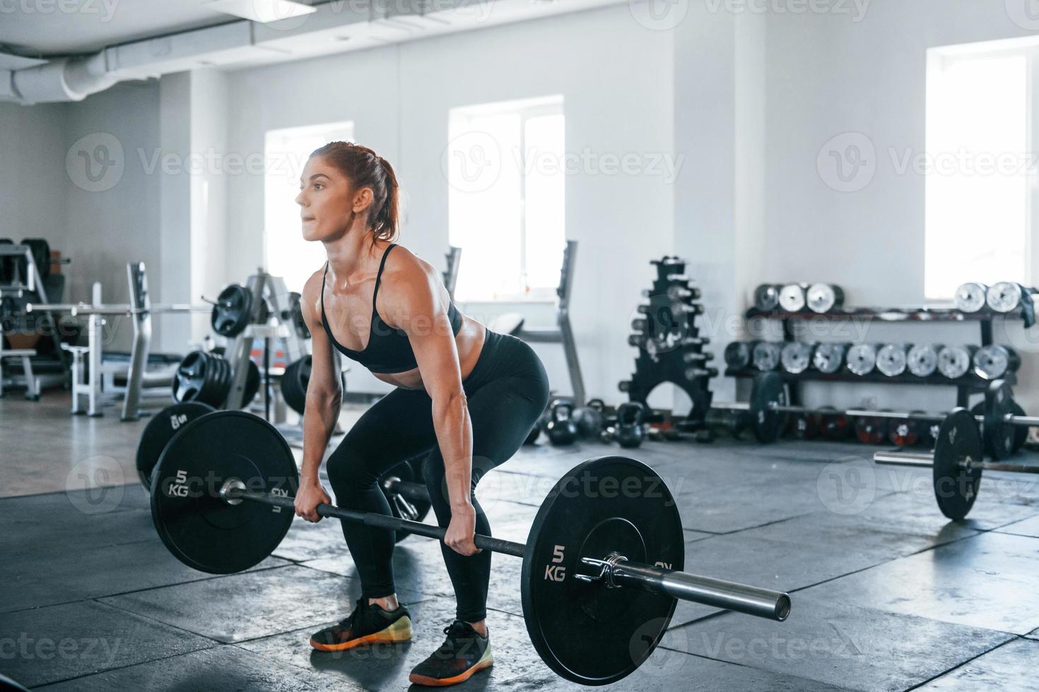 Young fitness woman with slim type of body doing exercises by using barbell photo