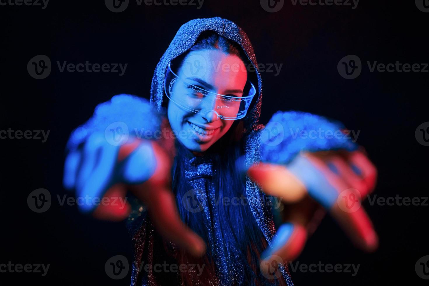 Does gestures by hands. Portrait of young girl that is in eyeglasses in blue neon lighting photo