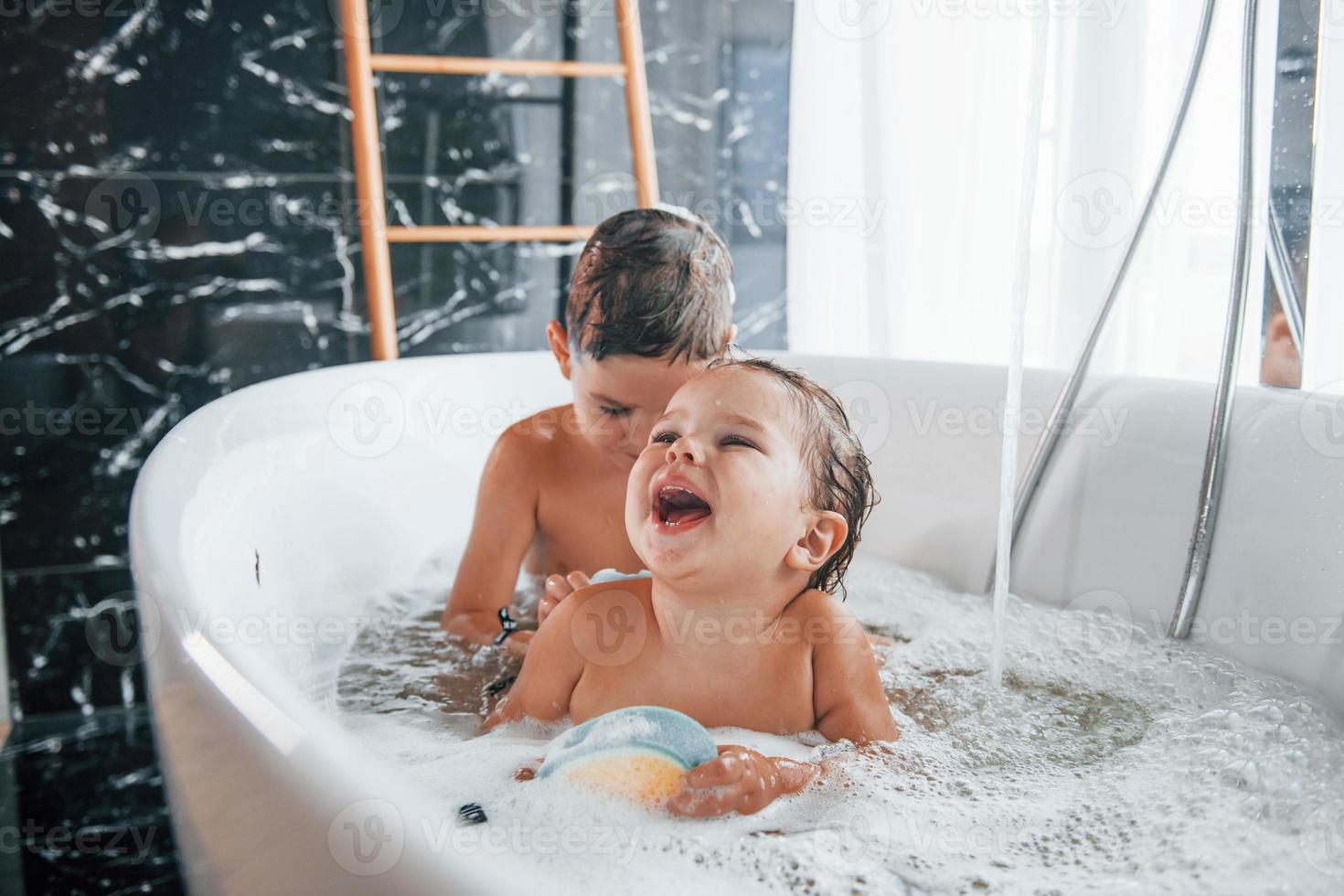 dos niños divirtiéndose y lavándose en el baño en casa. Ayudándose unos a otros foto