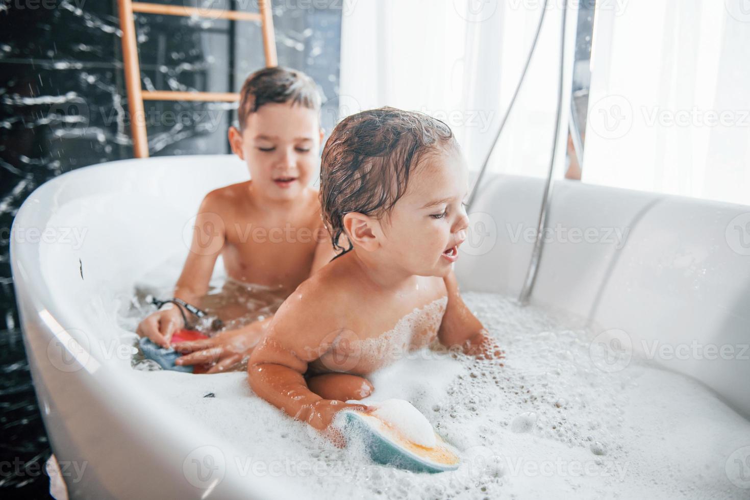 Two kids having fun and washing themselves in the bath at home. Helping each other photo