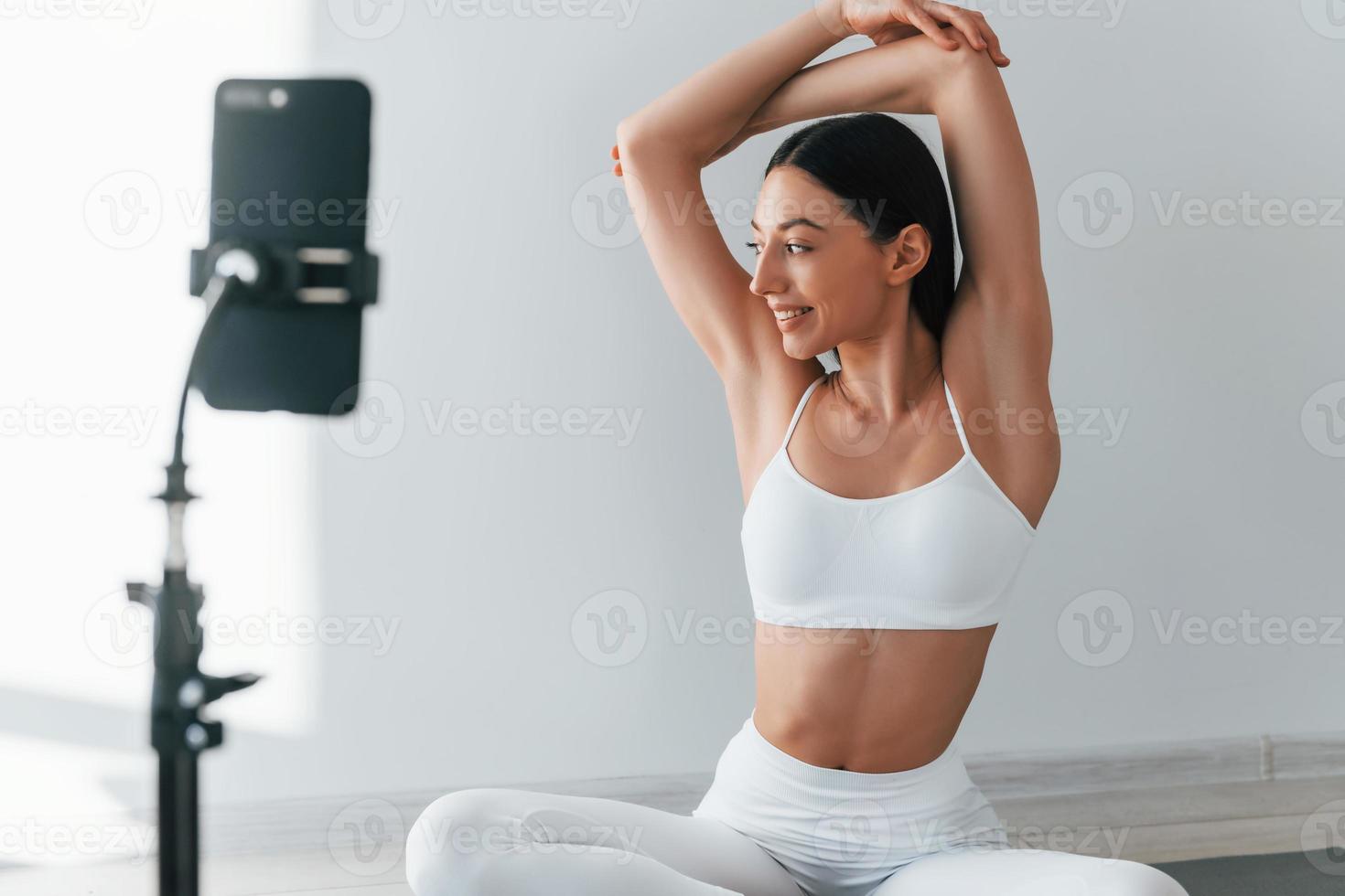 Phone on tripod. Young caucasian woman with slim body shape is indoors at daytime photo