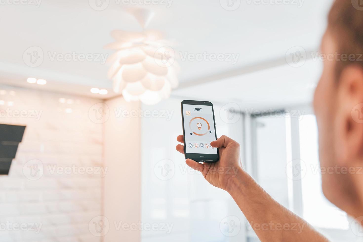 Holds phone. Rear view of adult man that is indoors controlling smart home technology photo