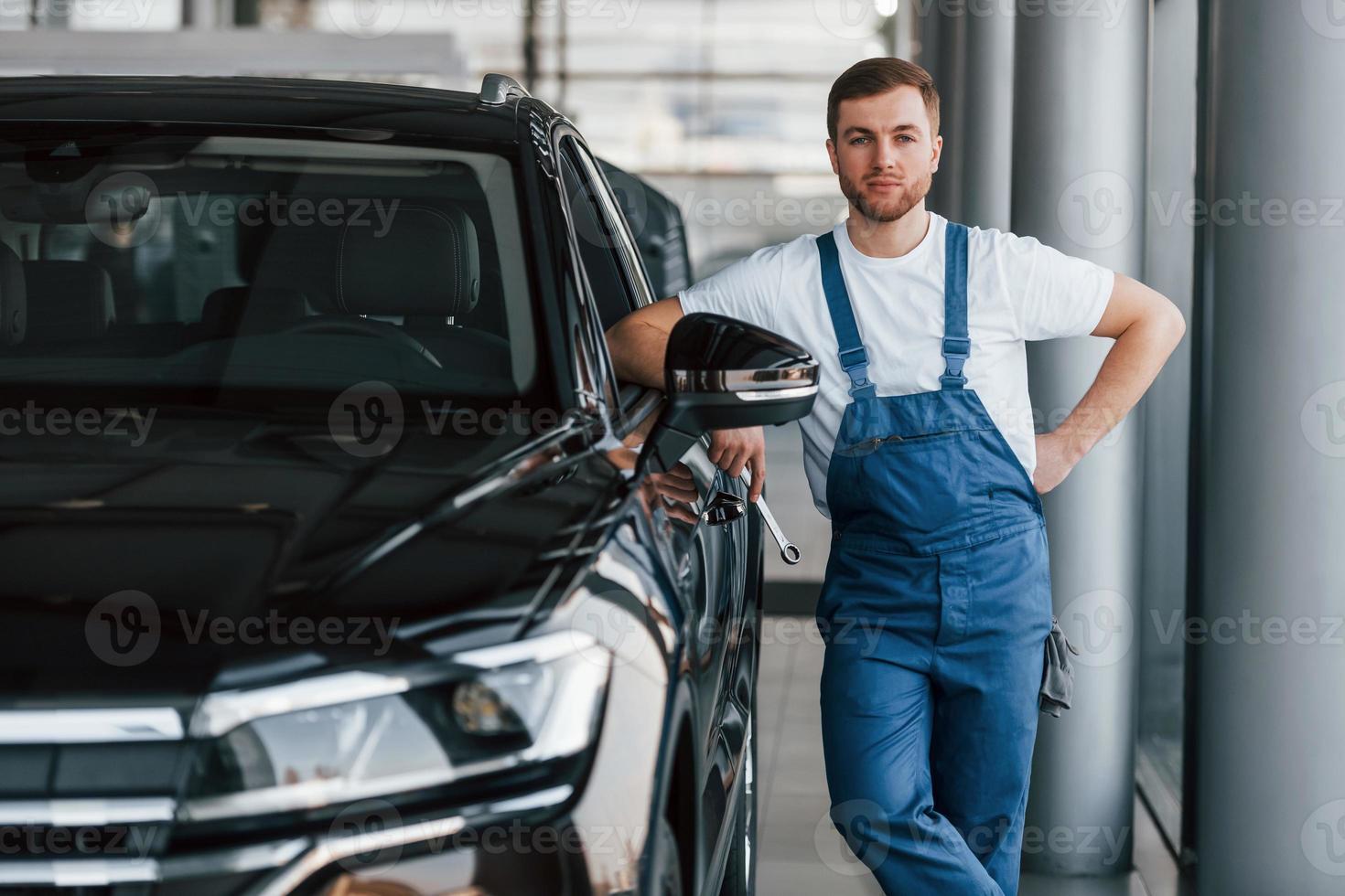 Front view of the car. Young man in white shirt and blue uniform repairs automobile photo