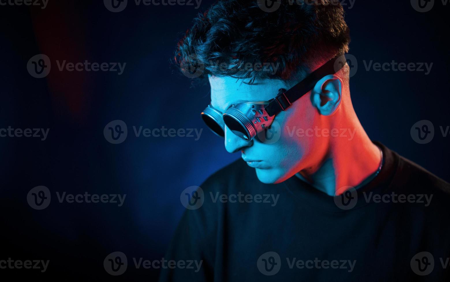 Against black background. Neon lighting. Young european man is in the dark studio photo