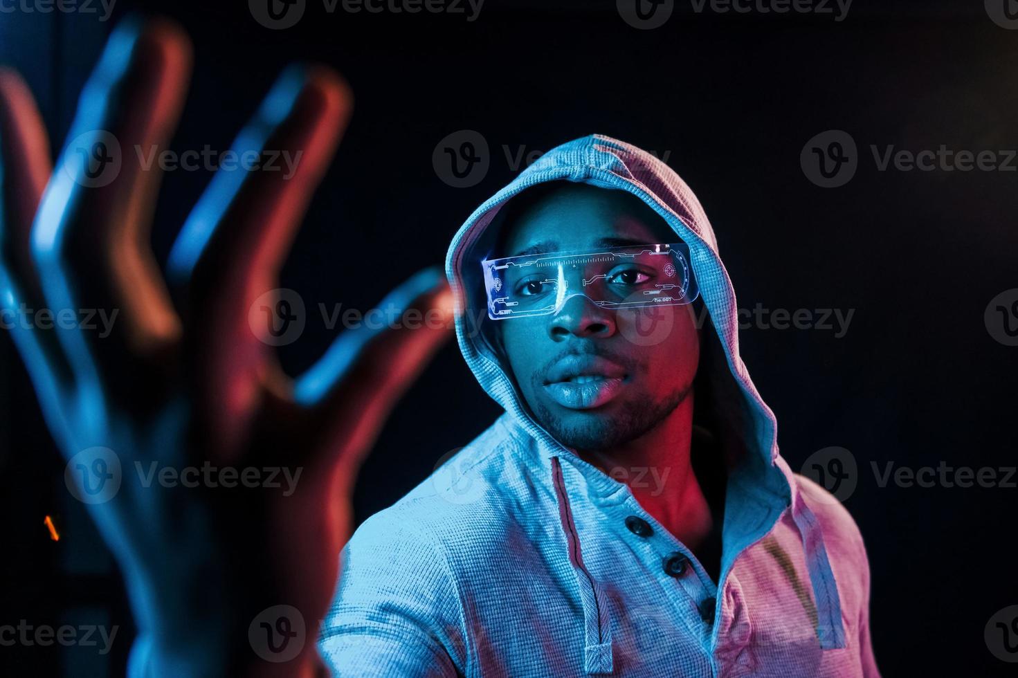 In special eyewear. Futuristic neon lighting. Young african american man in the studio photo