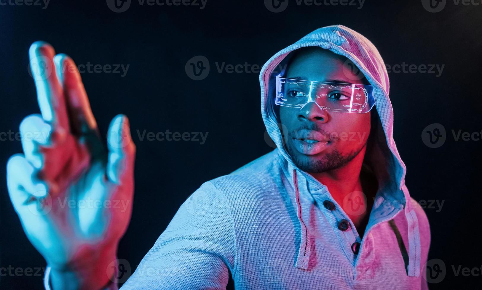 In special eyewear. Futuristic neon lighting. Young african american man in the studio photo