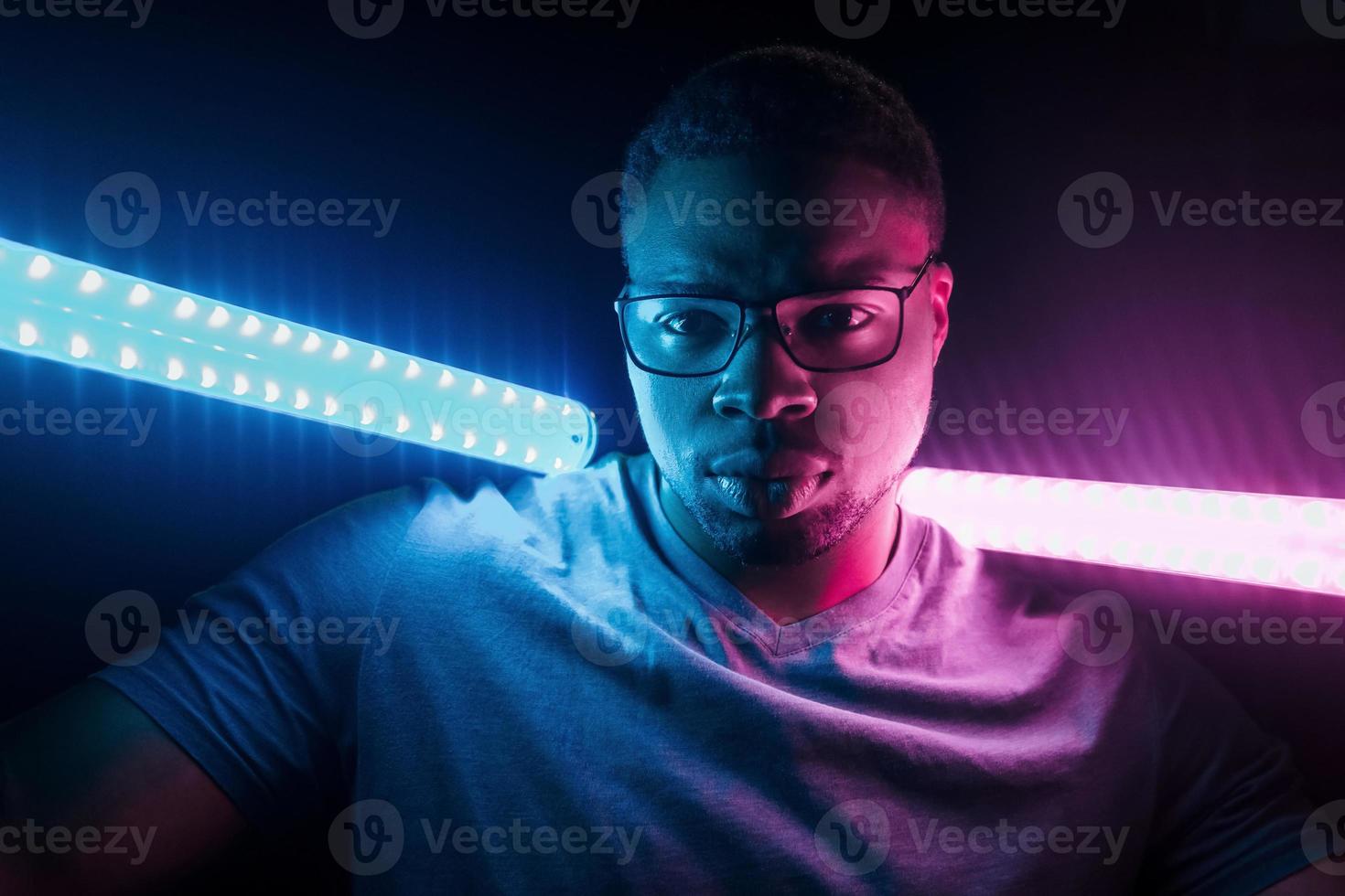 Holds lighting equipment. Futuristic neon lighting. Young african american man in the studio photo