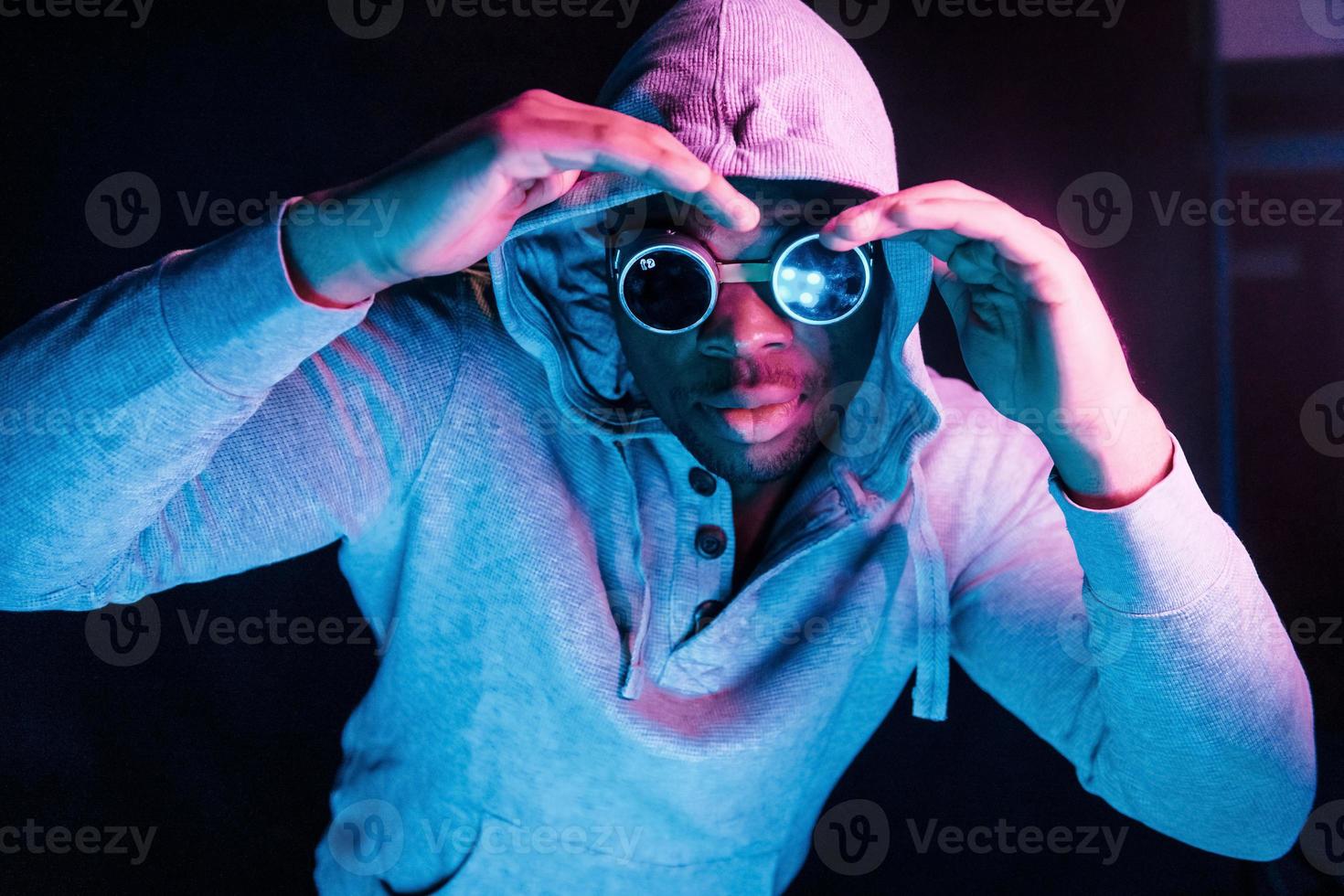 Cyberpunk style glasses. Futuristic neon lighting. Young african american man in the studio photo