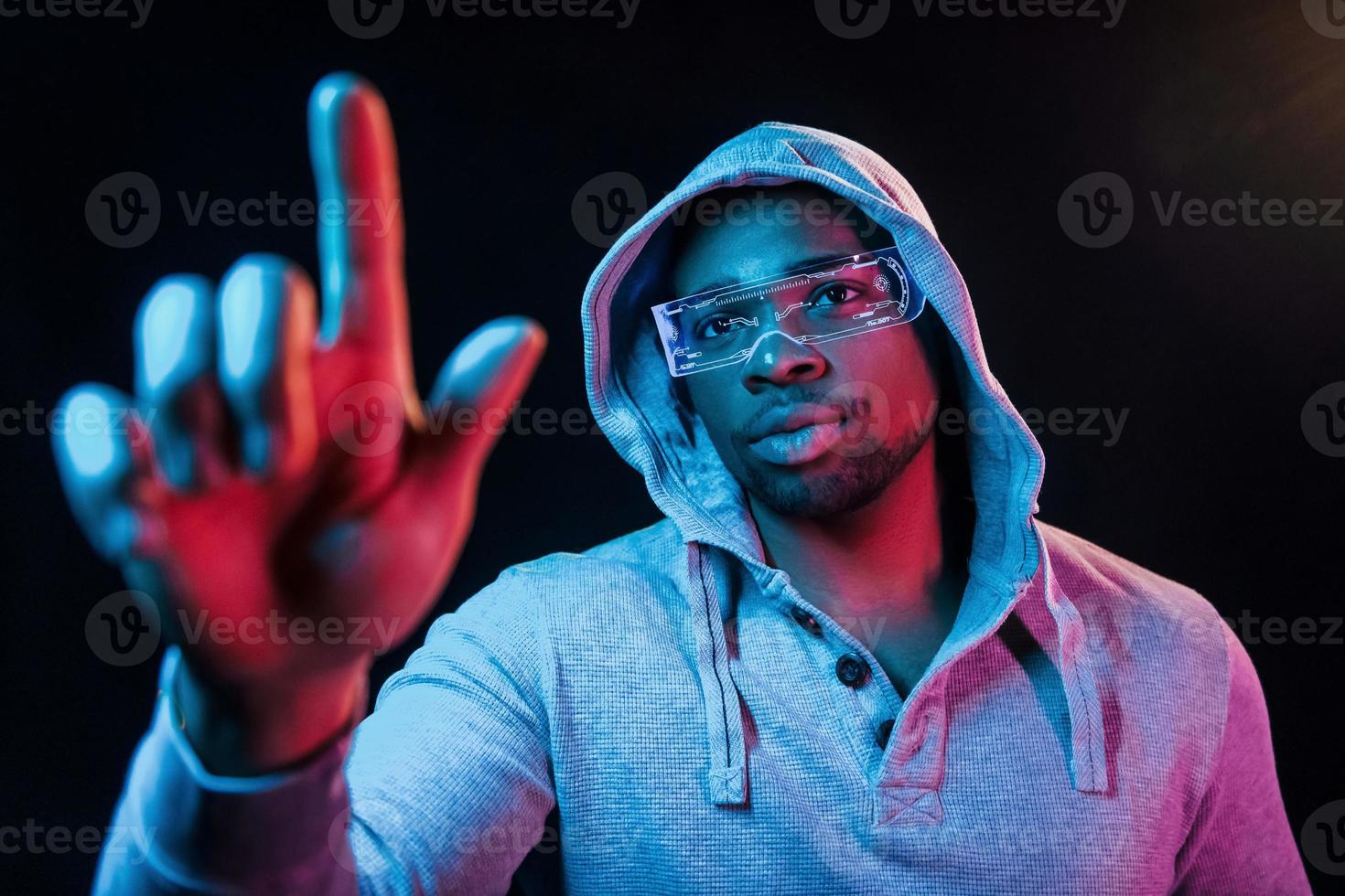 In special eyewear. Futuristic neon lighting. Young african american man in the studio photo