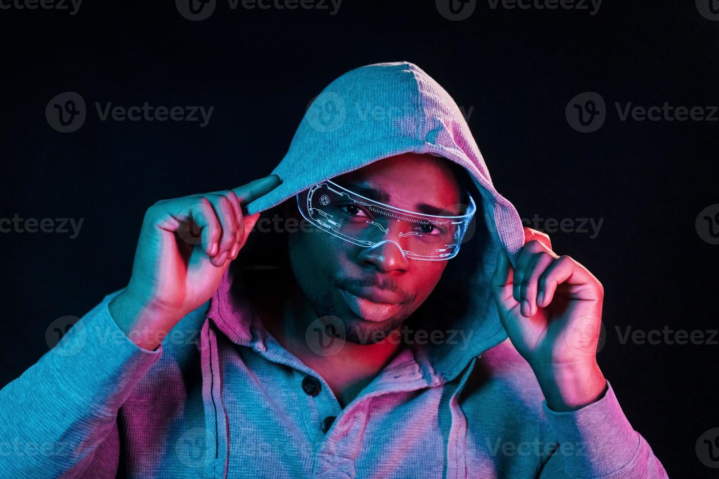 In special eyewear. Futuristic neon lighting. Young african american man in the studio photo