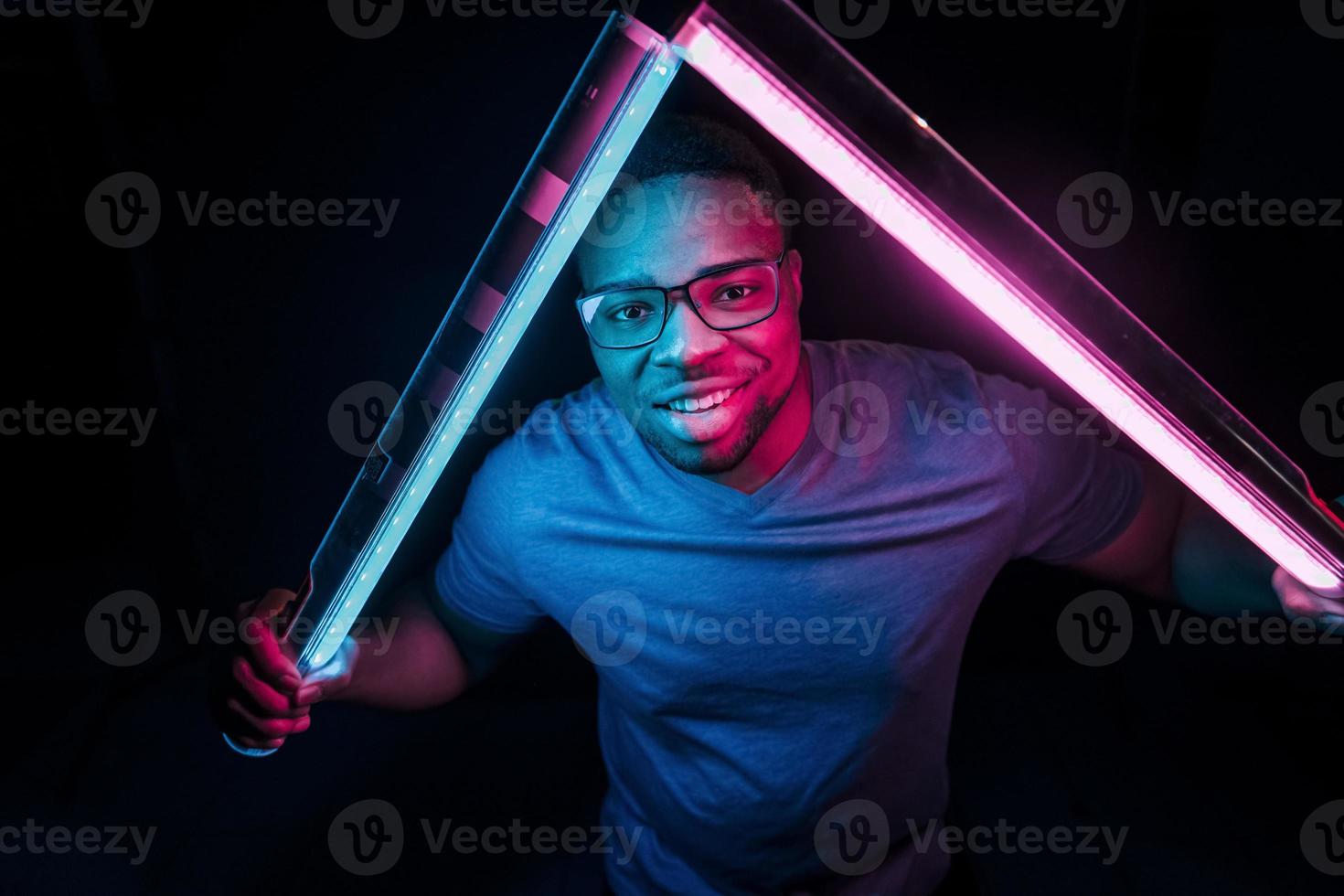 sostiene el equipo de iluminación. iluminación de neón futurista. joven afroamericano en el estudio foto