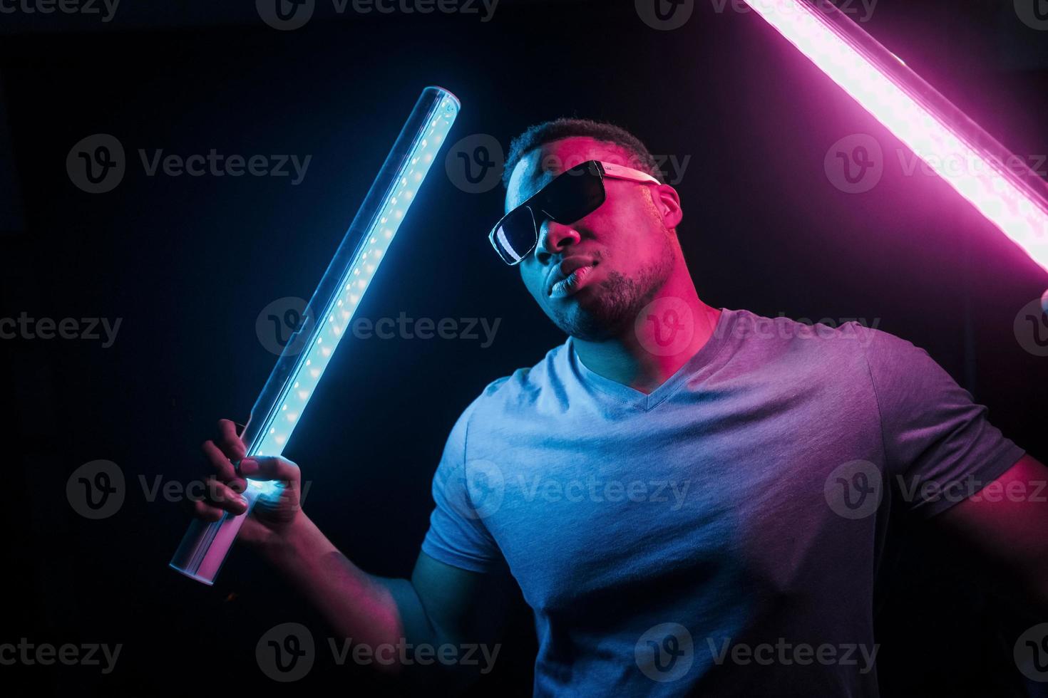 With sunglasses. Futuristic neon lighting. Young african american man in the studio photo