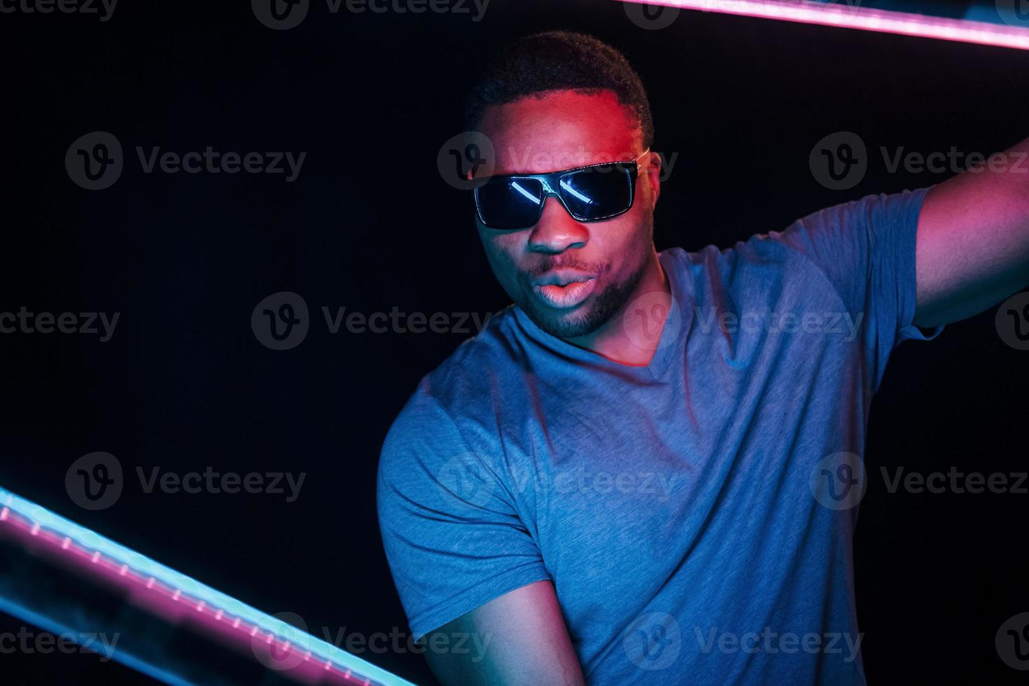 con gafas de sol iluminación de neón futurista. joven afroamericano en el estudio foto