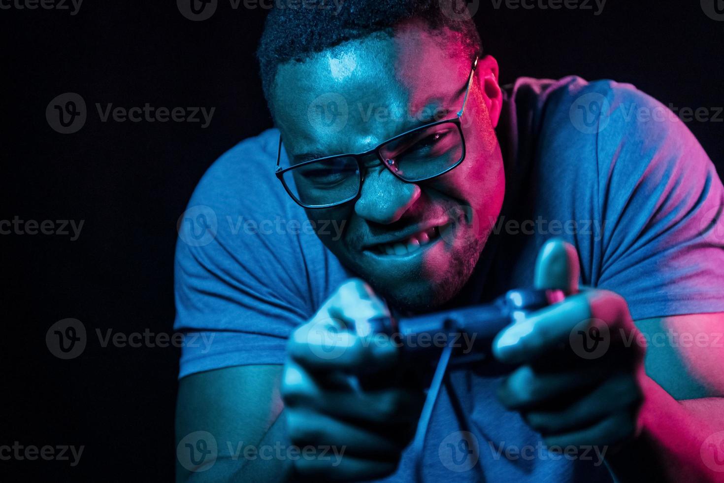 Plays game by using controller. Futuristic neon lighting. Young african american man in the studio photo