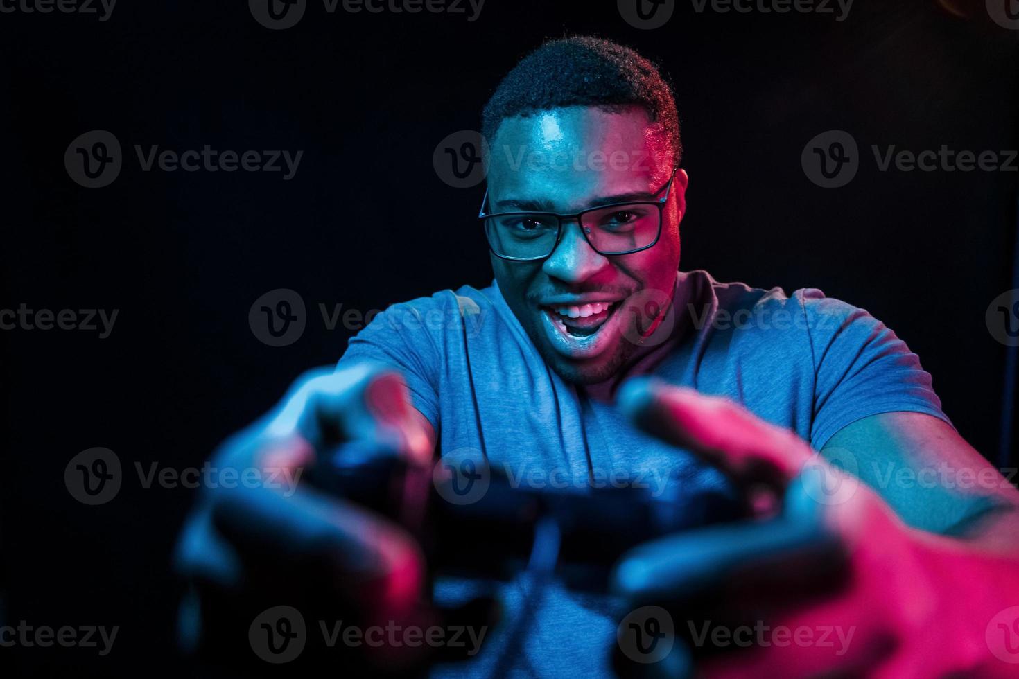 Plays game by using controller. Futuristic neon lighting. Young african american man in the studio photo