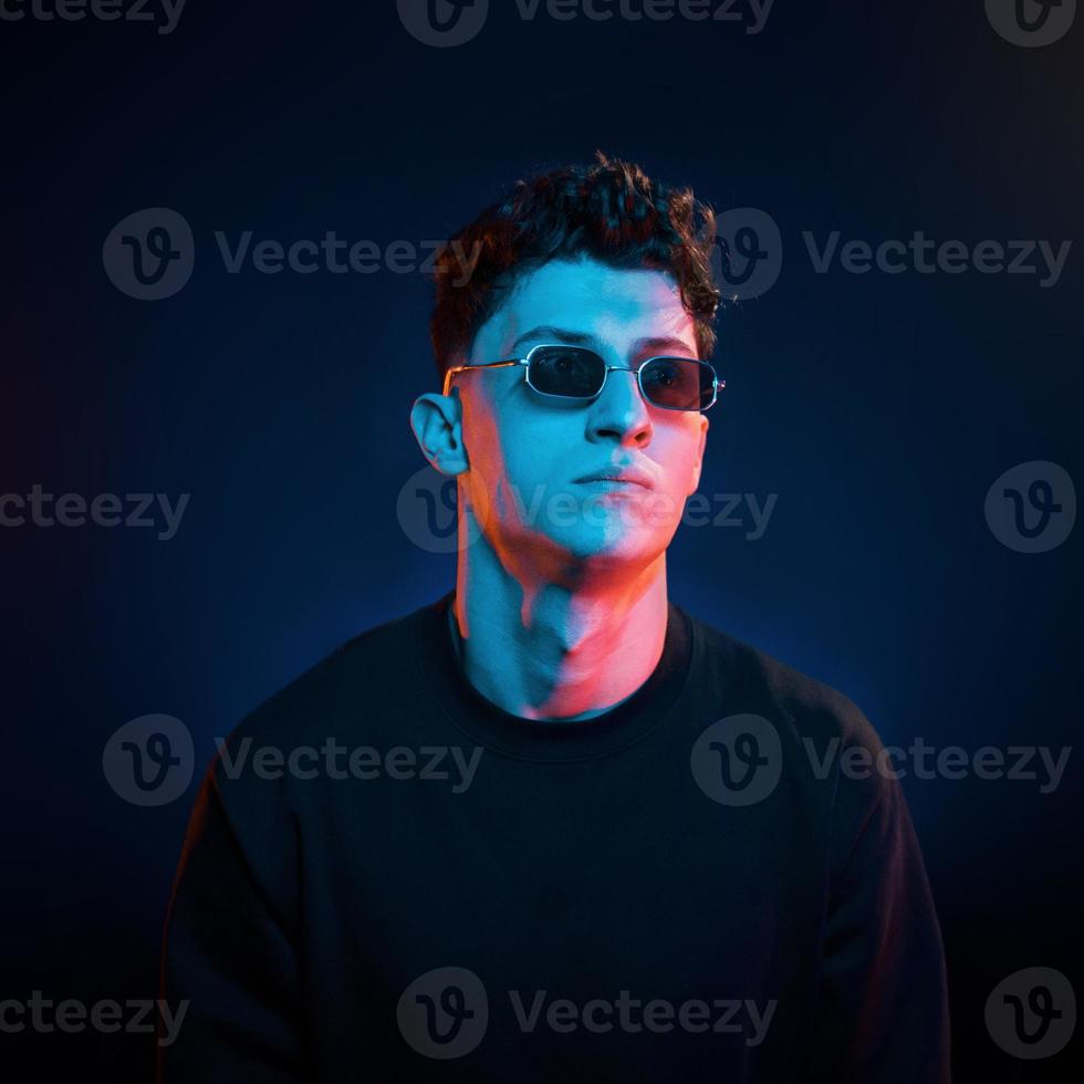 Stylish look. Neon lighting. Young european man is in the dark studio photo