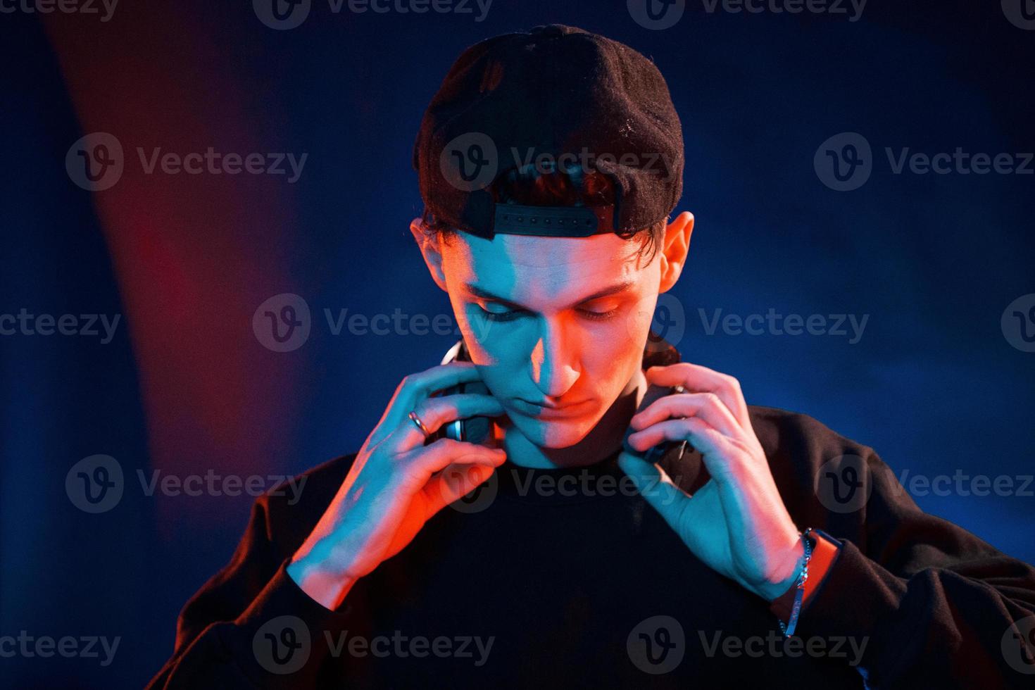 Guy uses headphones. Neon lighting. Young european man is in the dark studio photo
