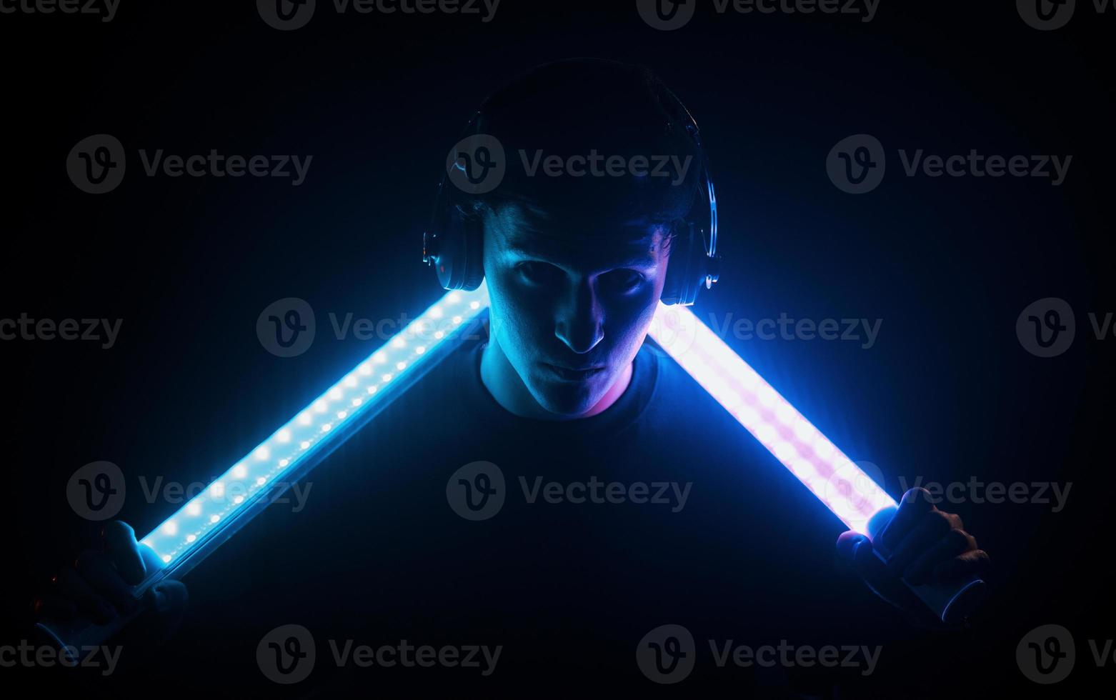 Guy uses headphones. Neon lighting. Young european man is in the dark studio photo