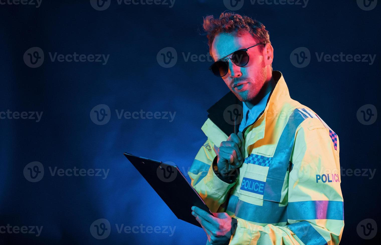 In police uniform. Neon lighting. Young european man is in the dark studio photo
