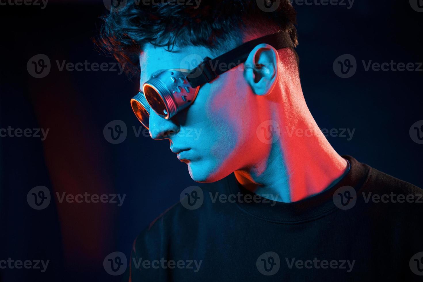 Against black background. Neon lighting. Young european man is in the dark studio photo