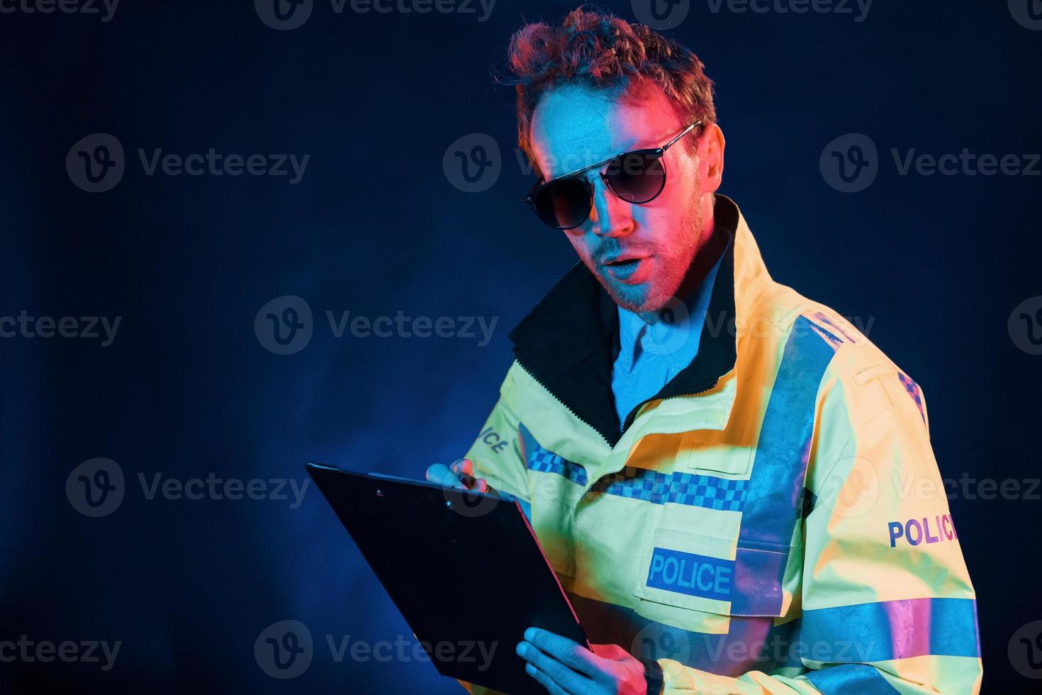 In police uniform. Neon lighting. Young european man is in the dark studio photo