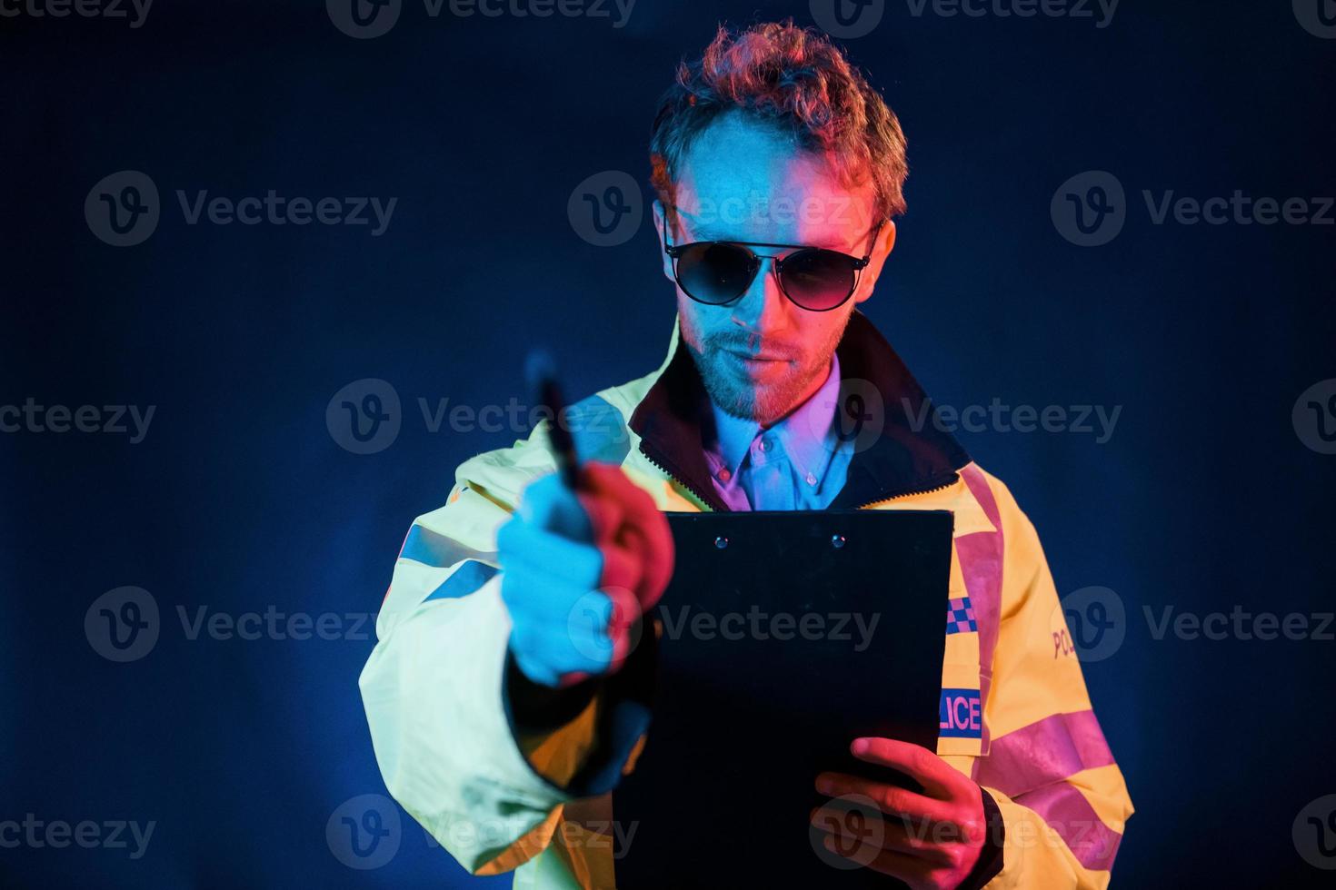 In police uniform. Neon lighting. Young european man is in the dark studio photo