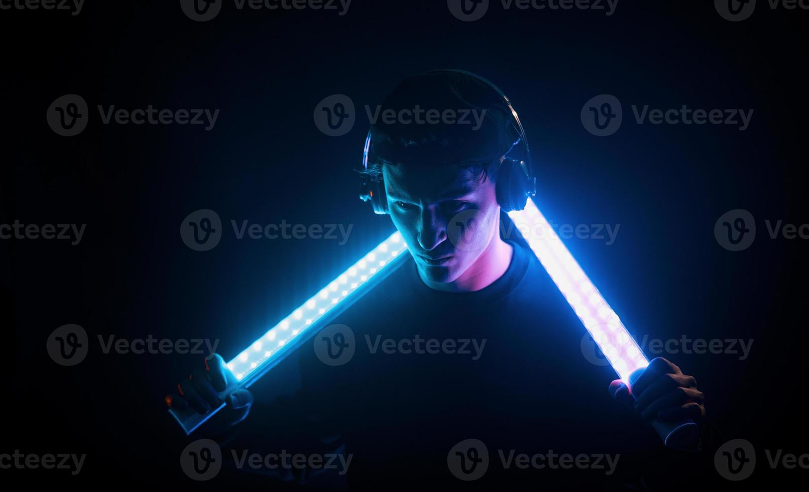 Guy uses headphones. Neon lighting. Young european man is in the dark studio photo