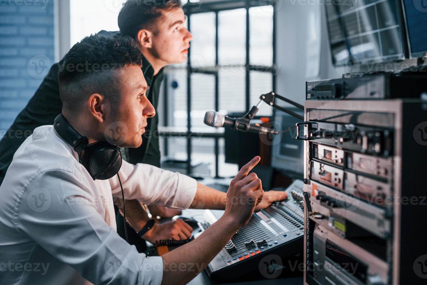 Conception of teamwork. Two guys is indoors in the radio studio is busy by broadcast photo