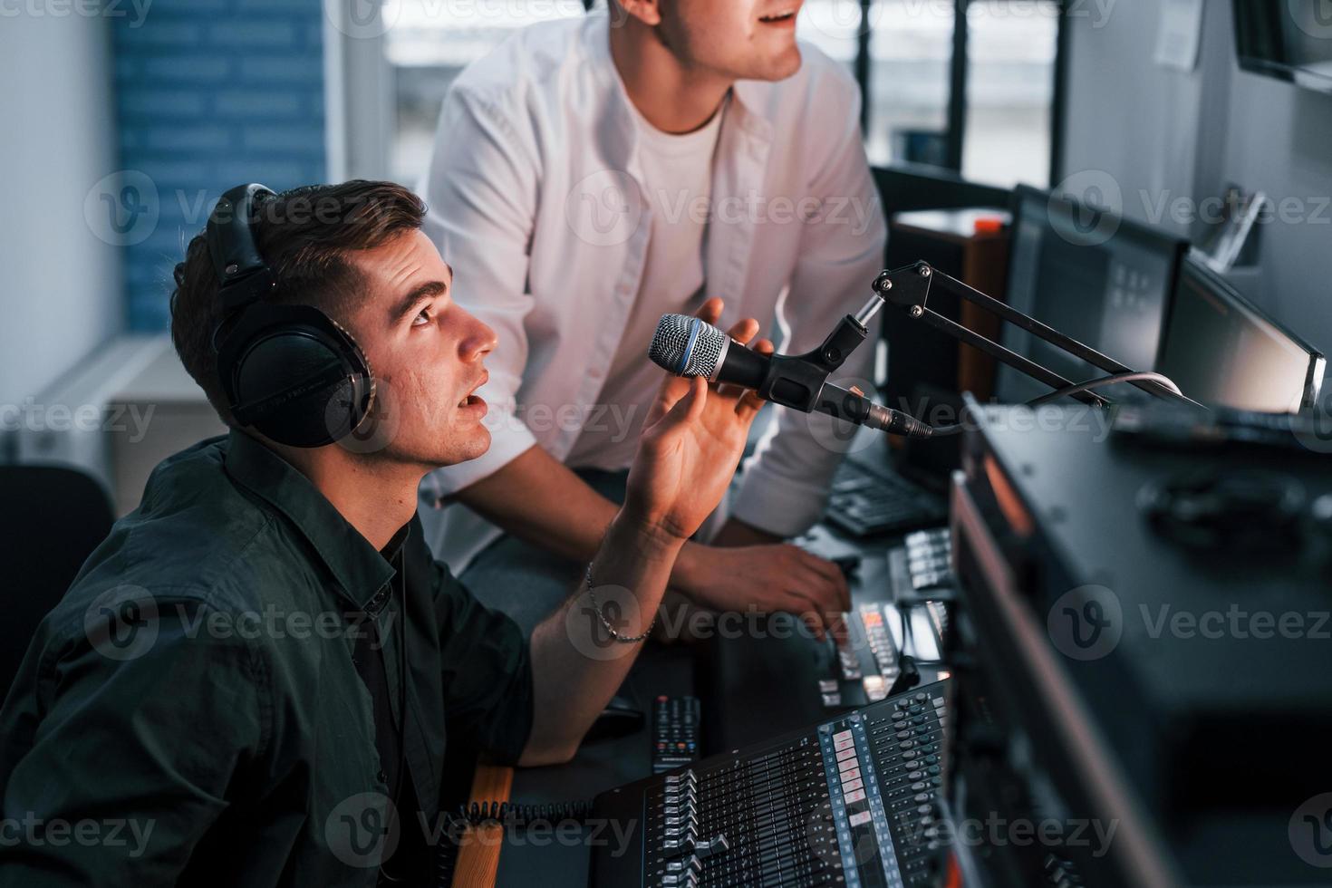 Conception of teamwork. Two guys is indoors in the radio studio is busy by broadcast photo