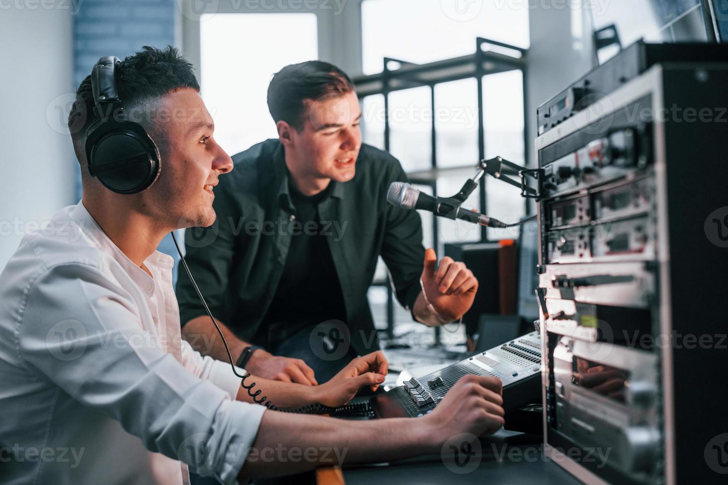 Conception of teamwork. Two guys is indoors in the radio studio is busy by broadcast photo