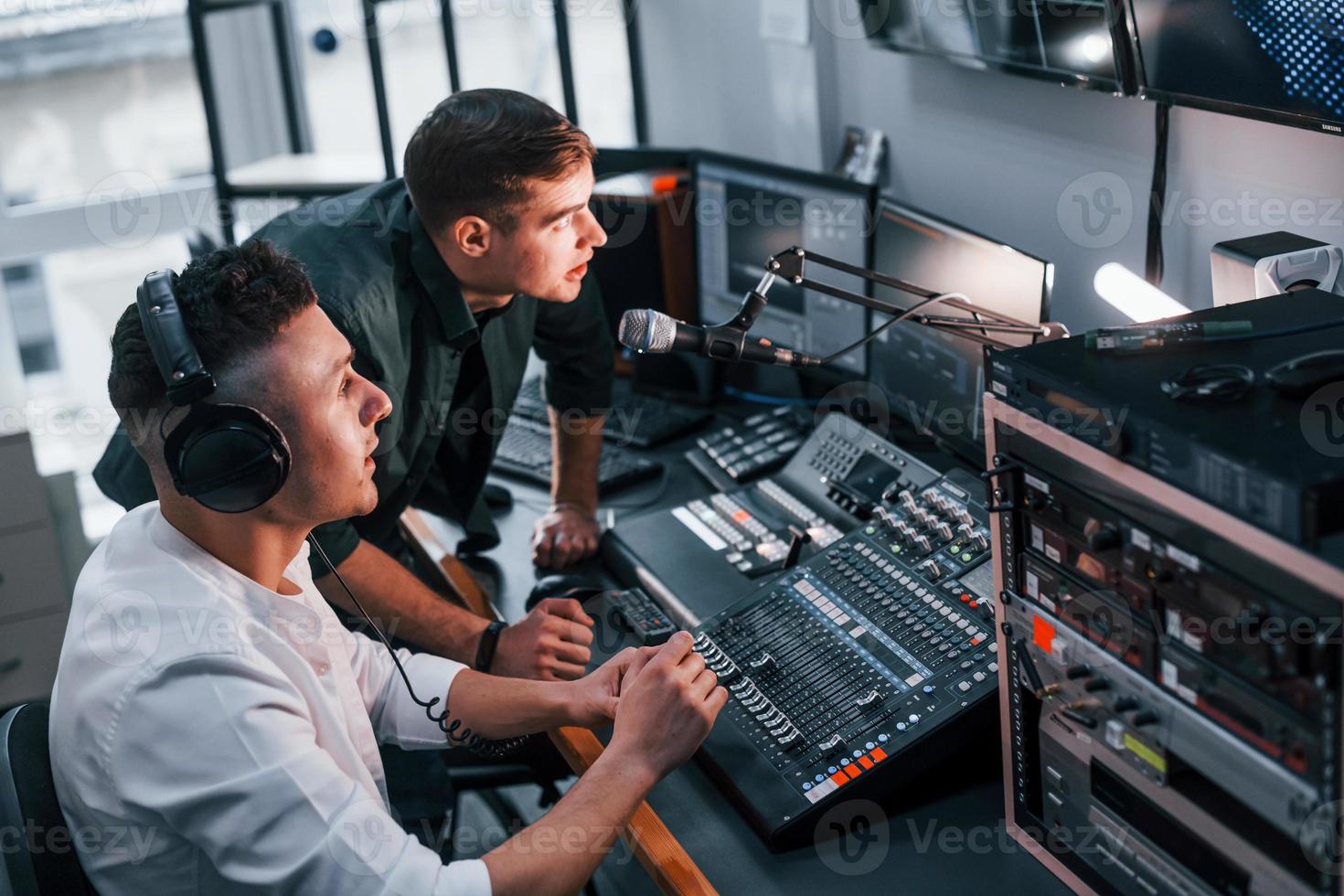 Conception of teamwork. Two guys is indoors in the radio studio is busy by broadcast photo