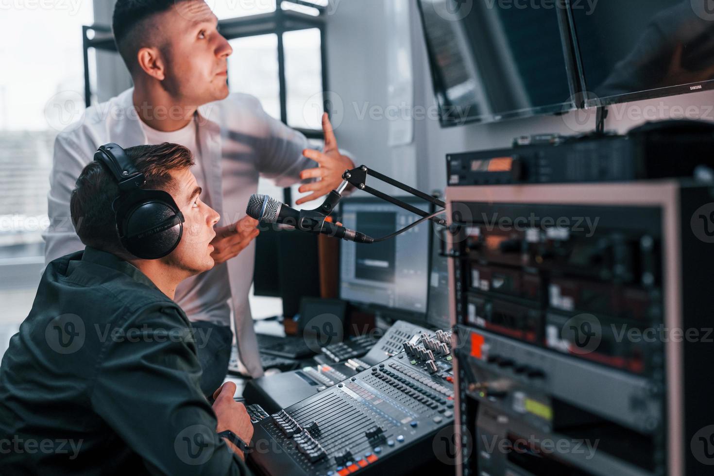 Conception of teamwork. Two guys is indoors in the radio studio is busy by broadcast photo