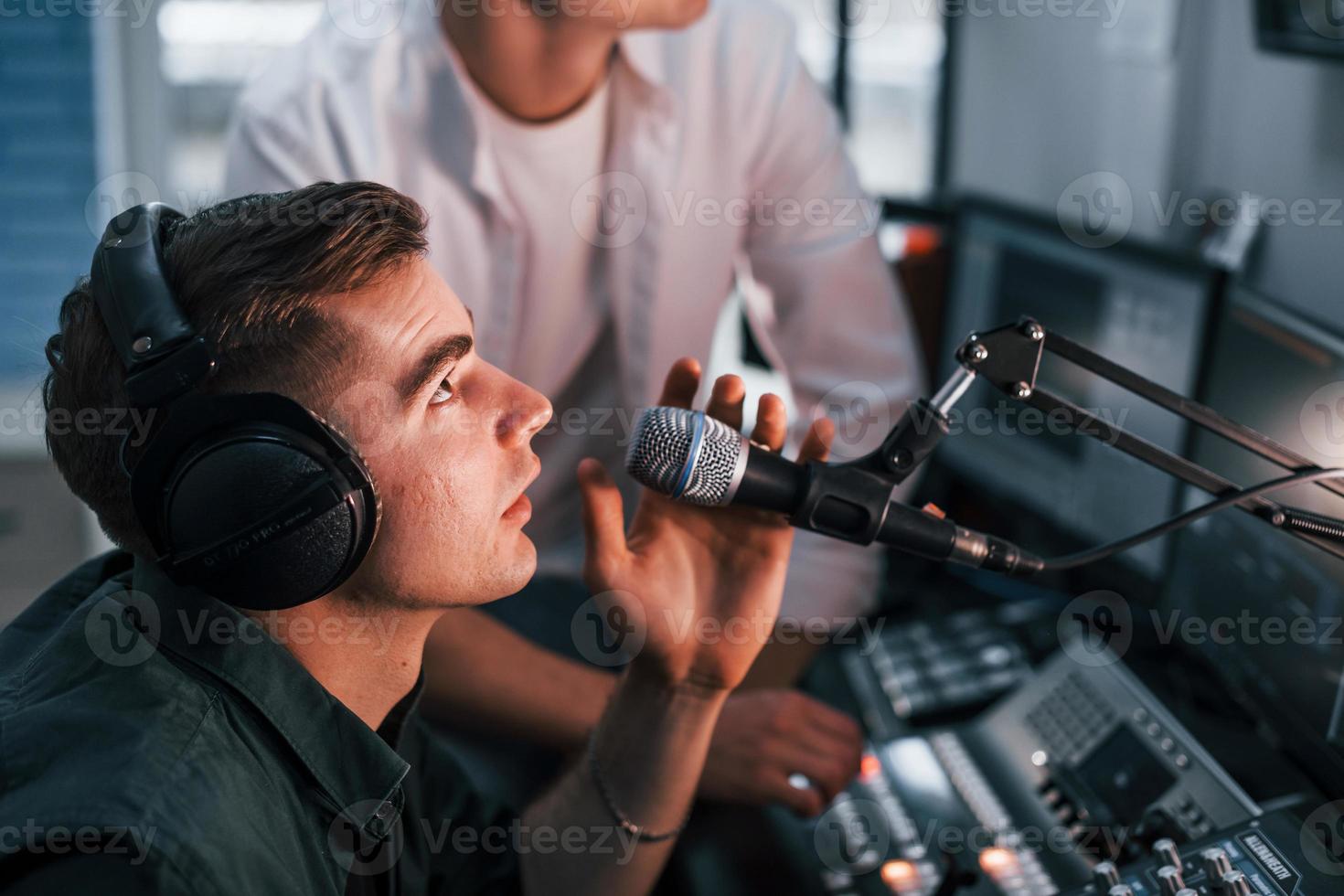 Conception of teamwork. Two guys is indoors in the radio studio is busy by broadcast photo