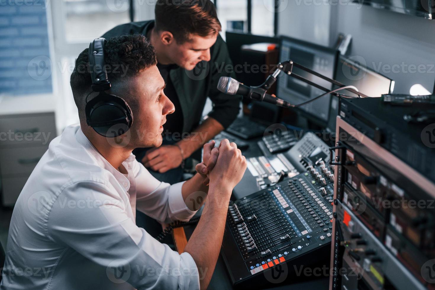 Conception of teamwork. Two guys is indoors in the radio studio is busy by broadcast photo