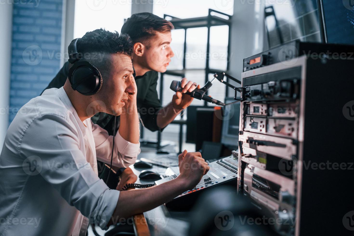 Conception of teamwork. Two guys is indoors in the radio studio is busy by broadcast photo