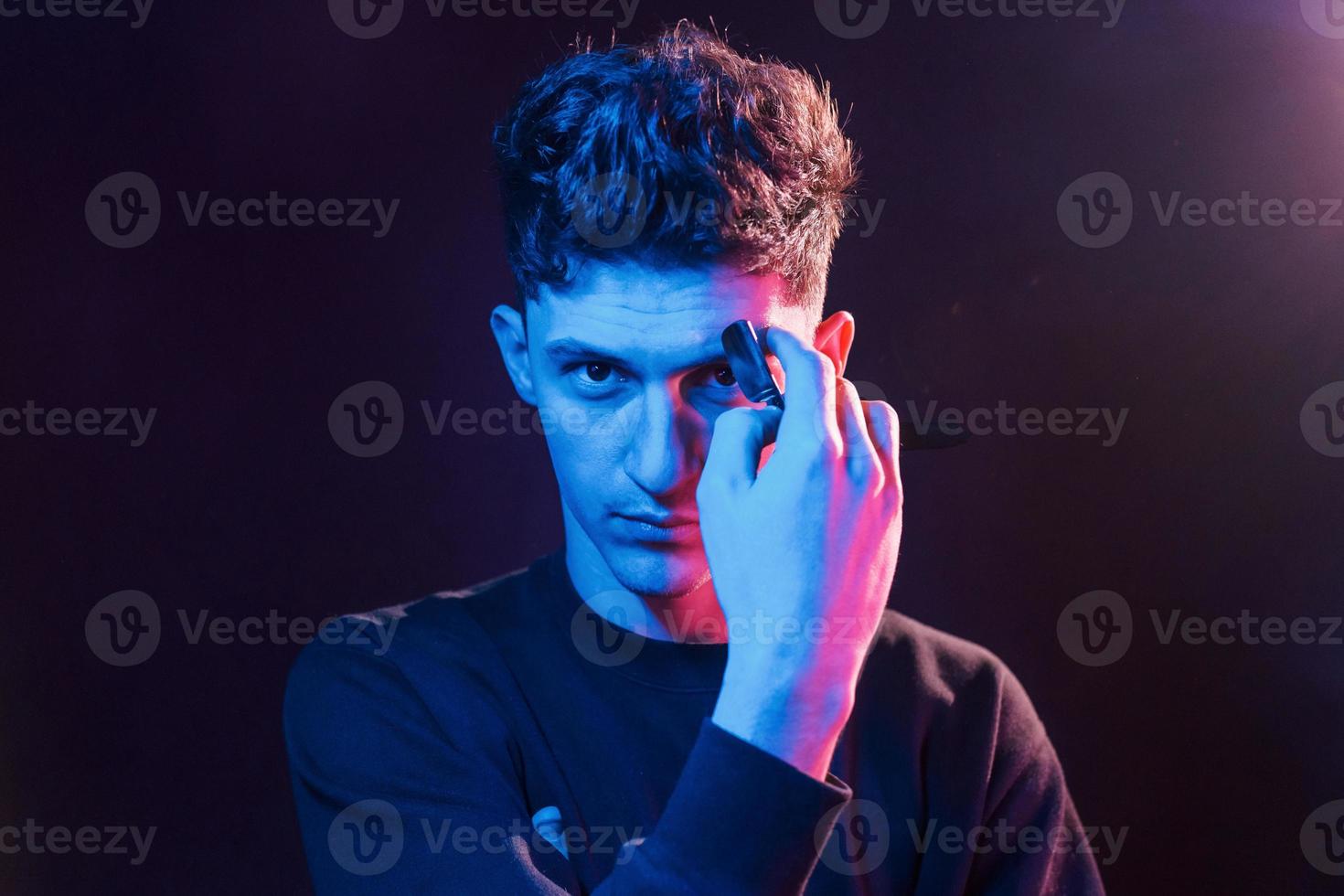 Young barber with work equipment standing in the studio with neon lighting photo