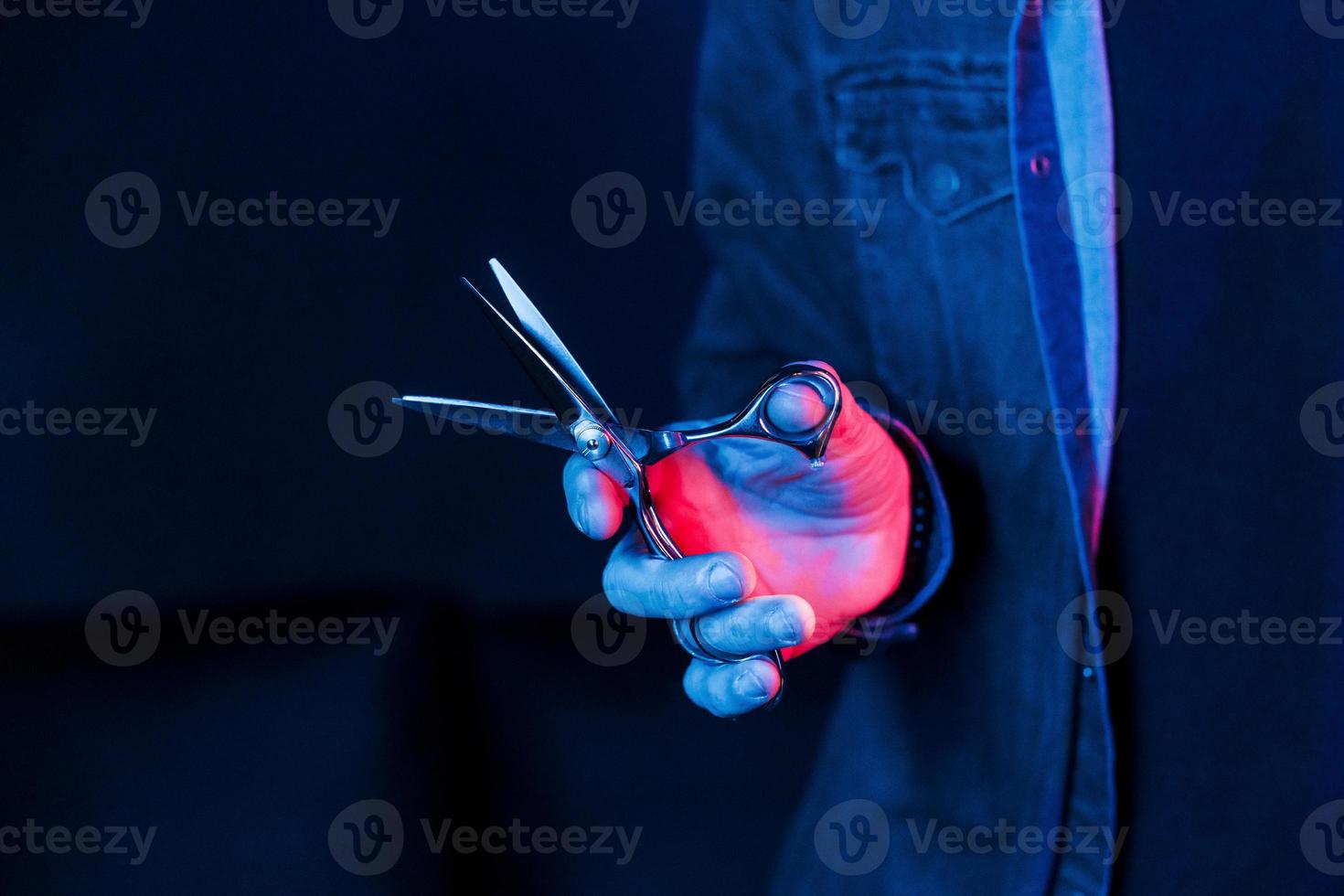 vista de cerca de las manos de barbero que sostienen tijeras. iluminación de neón foto