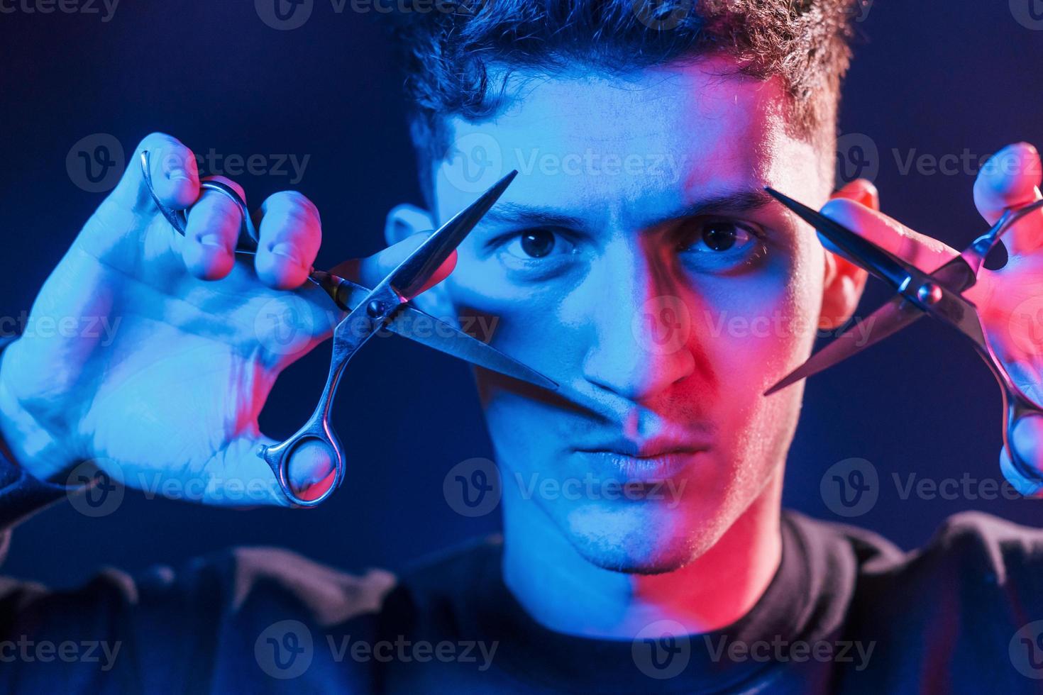 Holds scissors. Young barber with work equipment standing in the studio with neon lighting photo