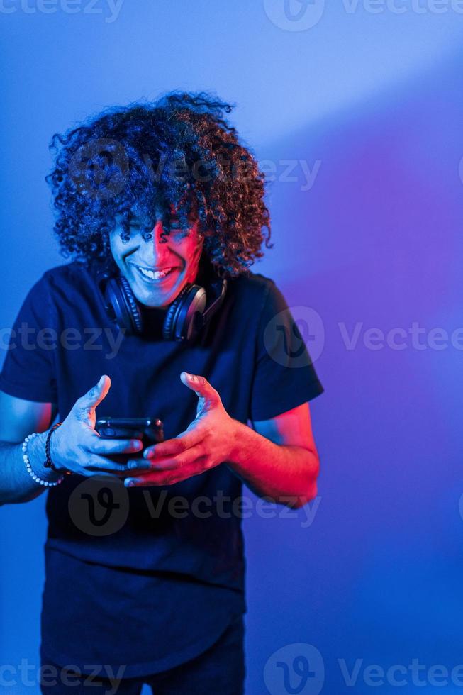 un joven hermoso con el pelo rizado está en el interior del estudio con luces de neón foto