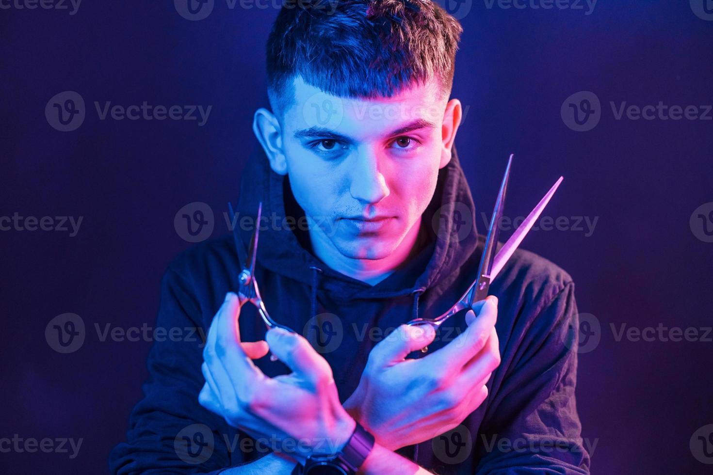 Holds scissors. Young barber with work equipment standing in the studio with neon lighting photo