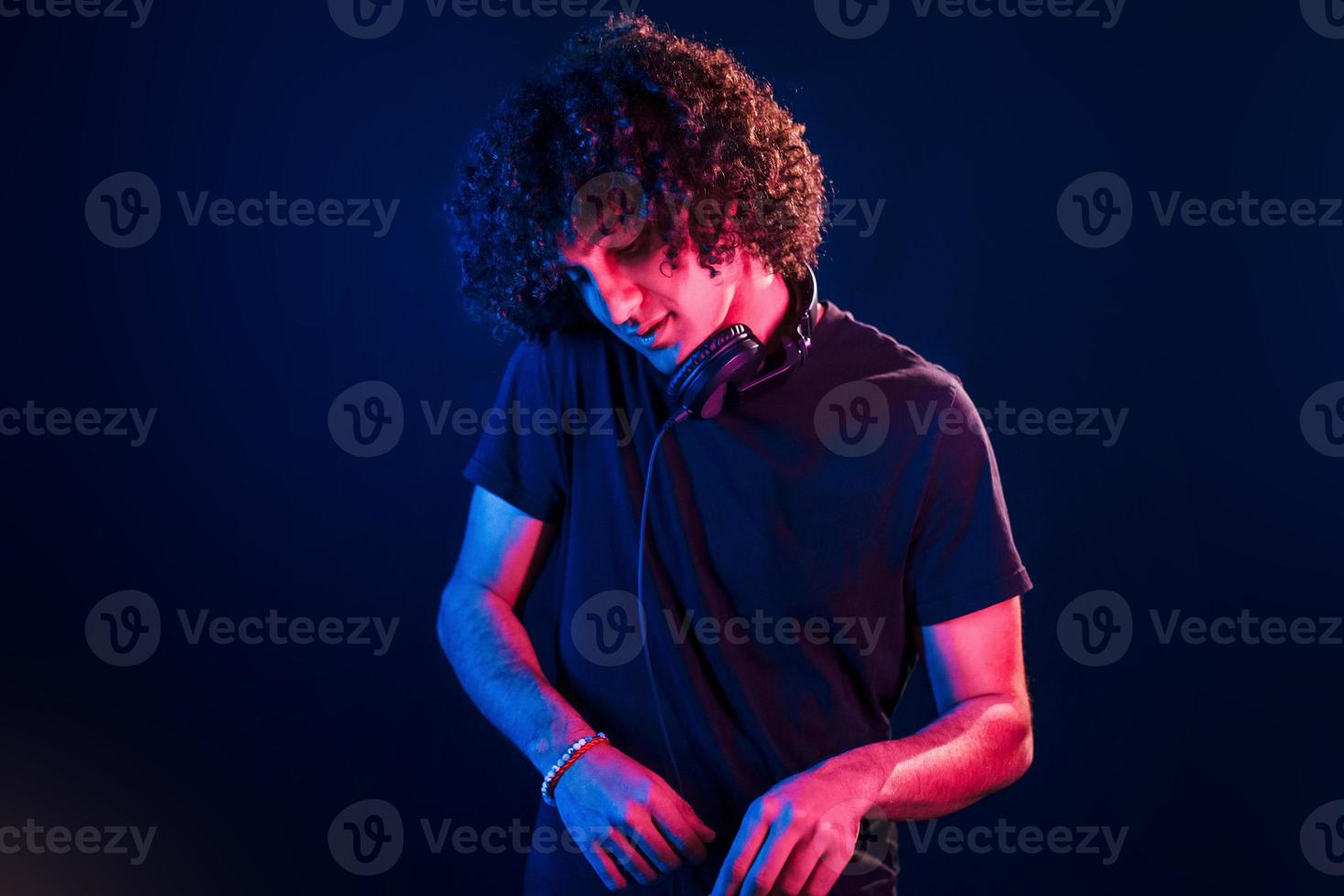 Young DJ with curly hair standing in the club with neon light photo