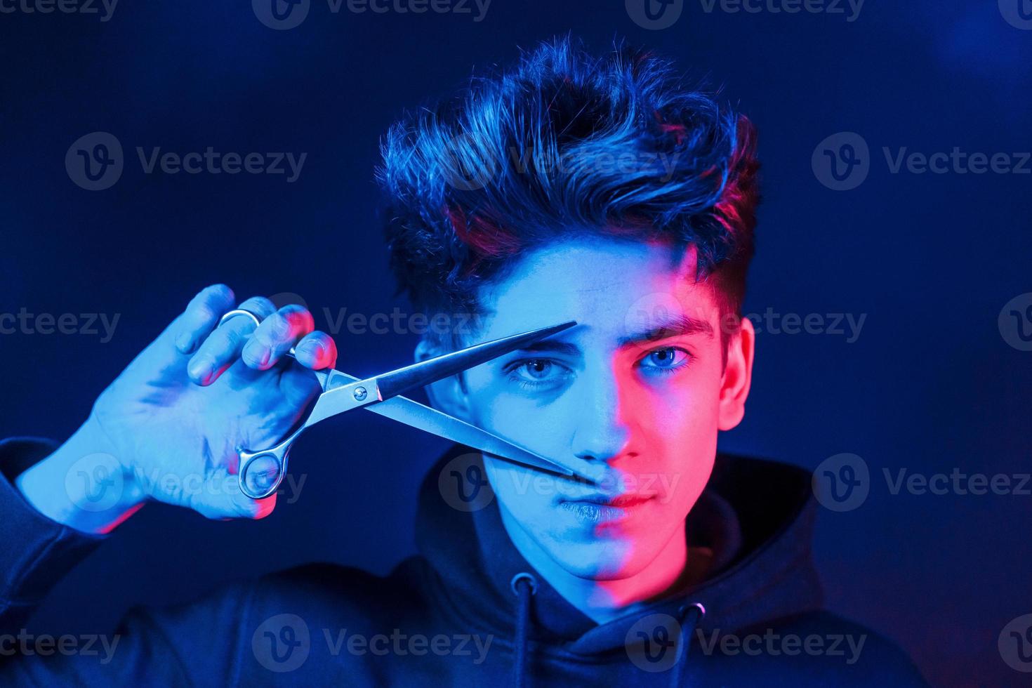 Holds scissors. Young barber with work equipment standing in the studio with neon lighting photo