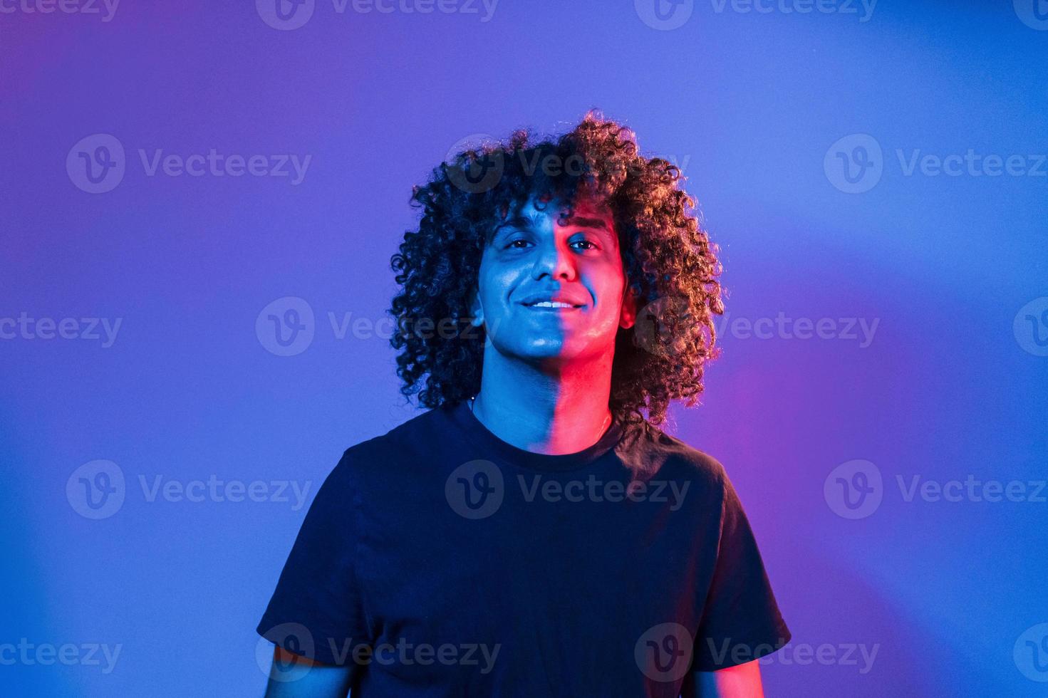 Young beautiful man with curly hair is indoors in the studio with neon lighting photo