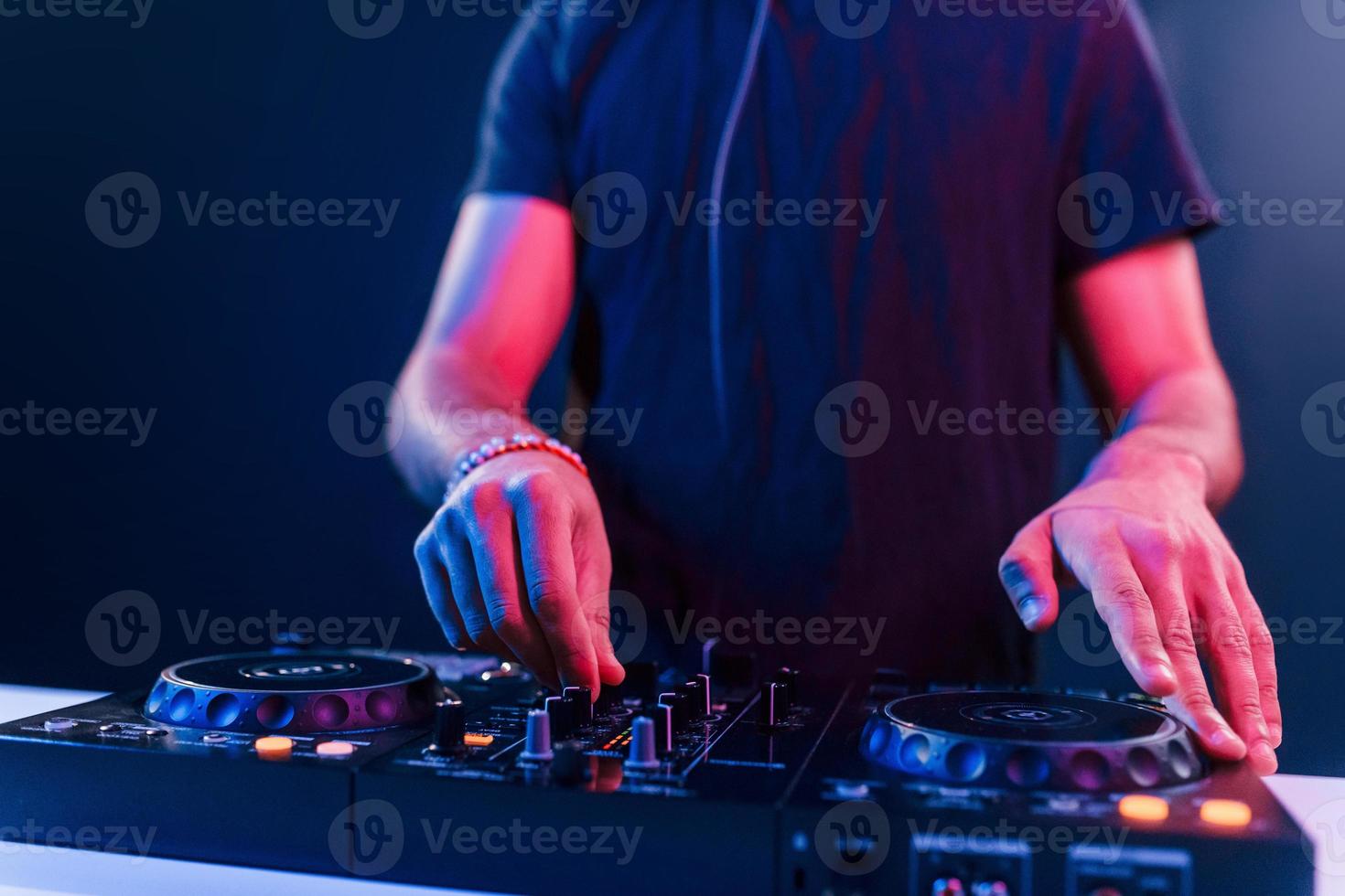 Close up view of DJ's hands that working with music equipment in the club with neon lighting photo